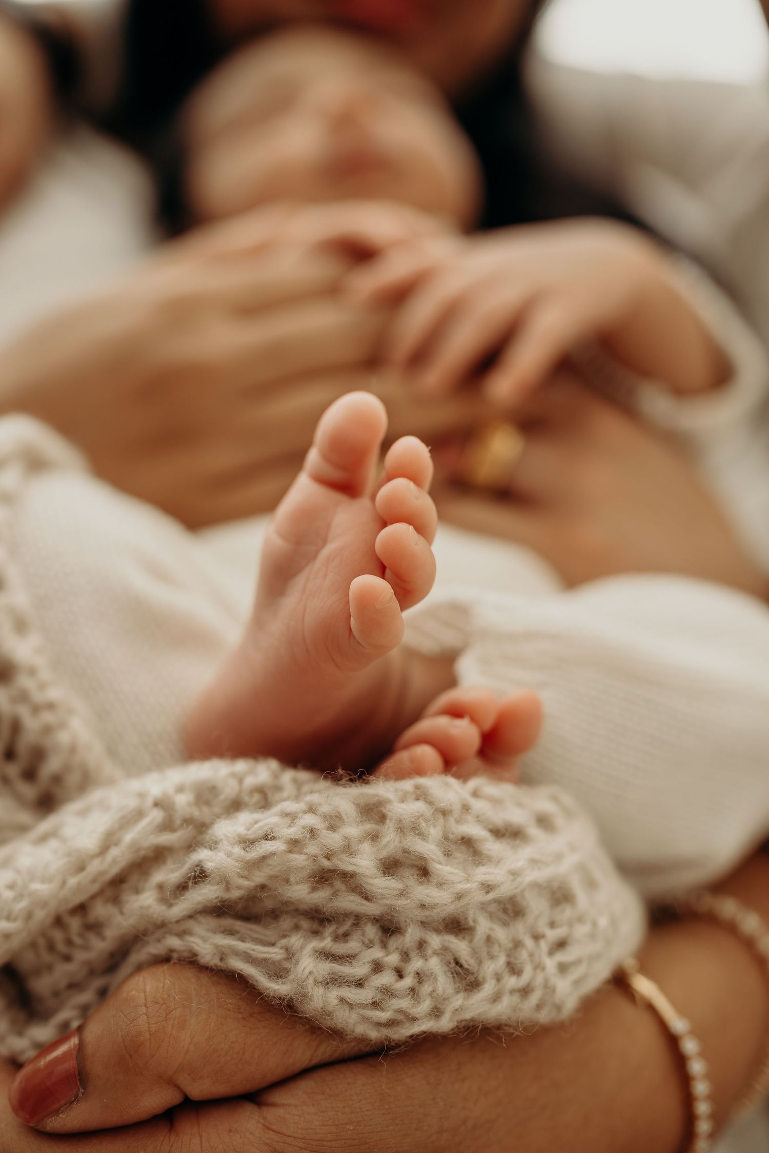 Close-up of a newborn baby's tiny feet resting in a mother's hands, wrapped in a soft knit blanket.