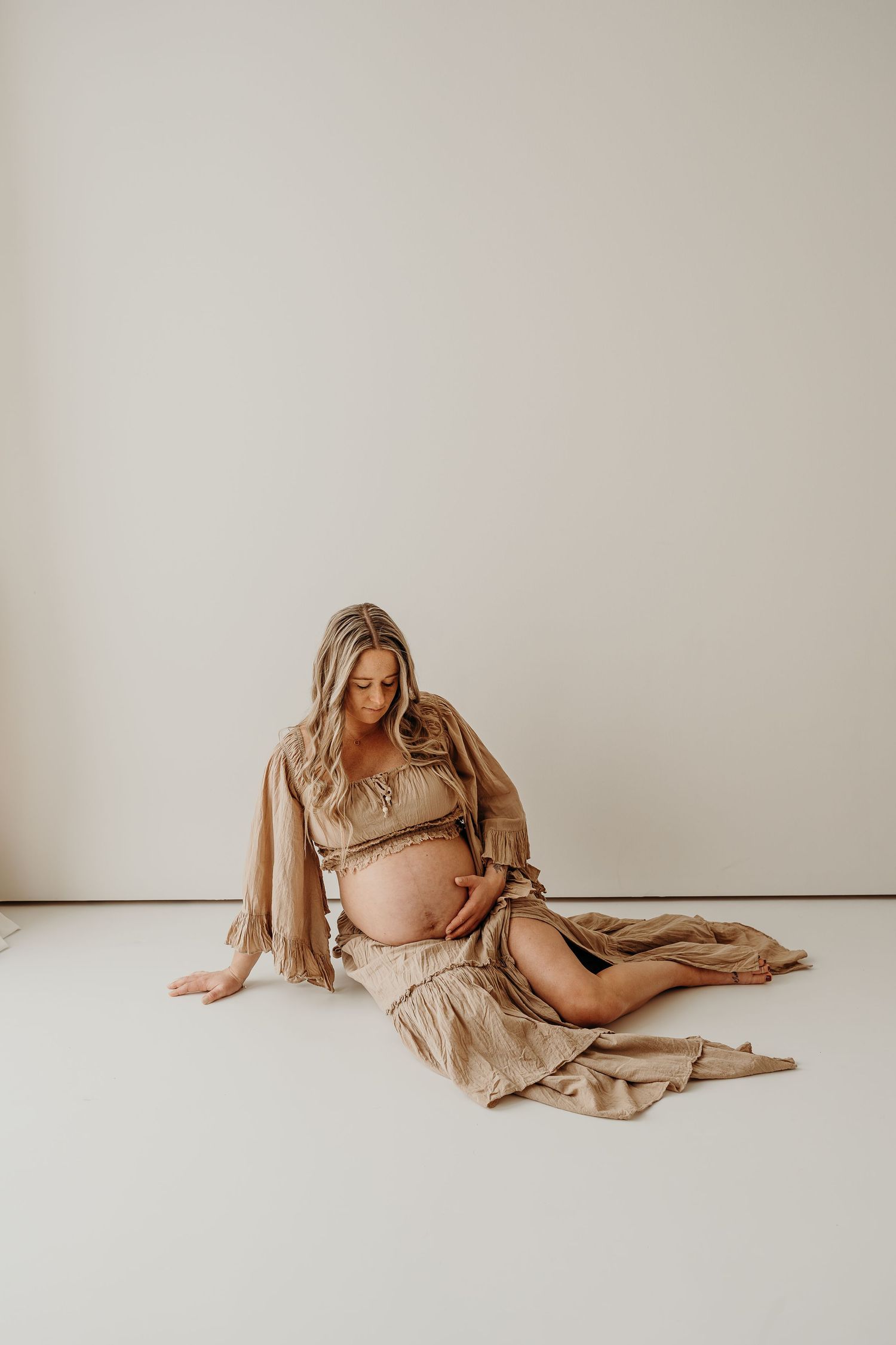 Artistic maternity photos in soft beige tones showing flowing fabric and gentle poses against white backdrop.