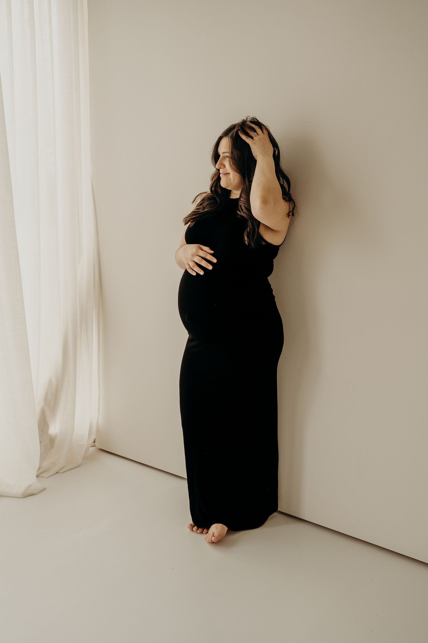 A series of minimalist photos showing a person in black clothing sitting against a white wall with flowing curtains.