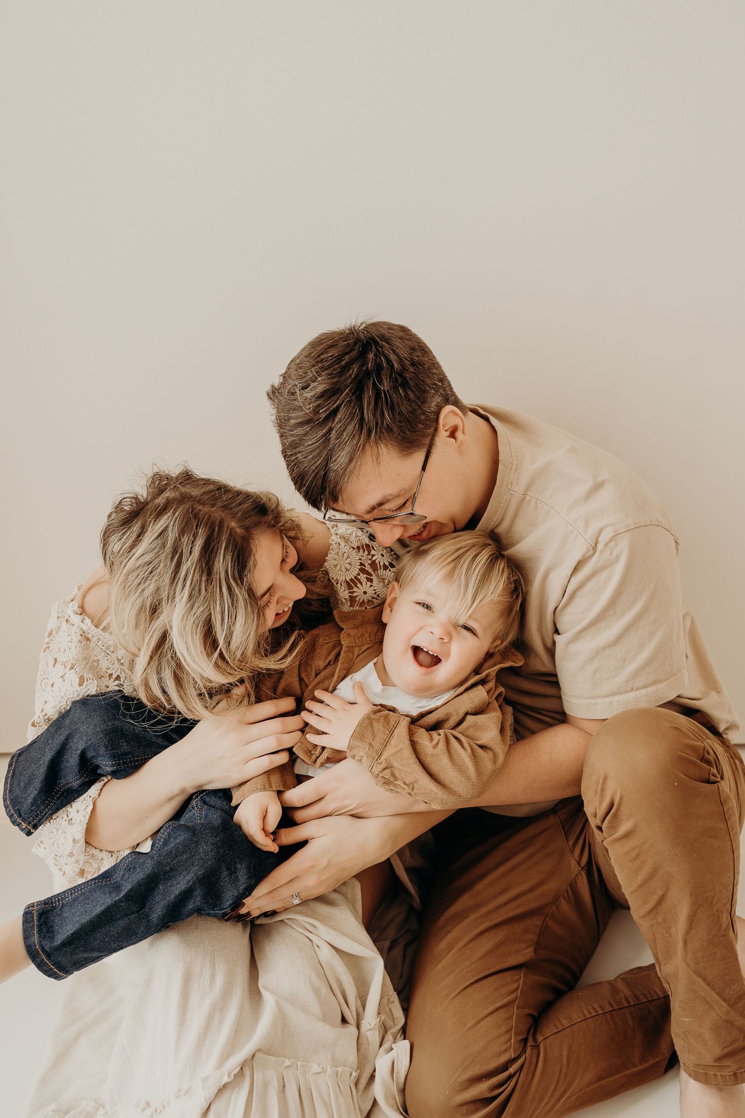 A joyful family of three shares a warm, candid moment as parents laugh with their happy toddler in a bright studio located in East Troy WI