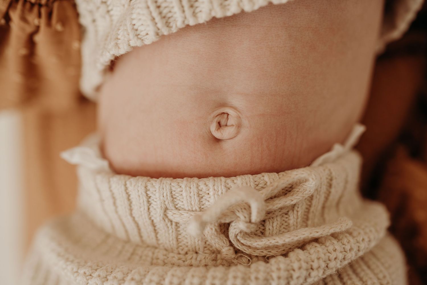 Close-up detail of a baby's belly button with white knitted clothing.