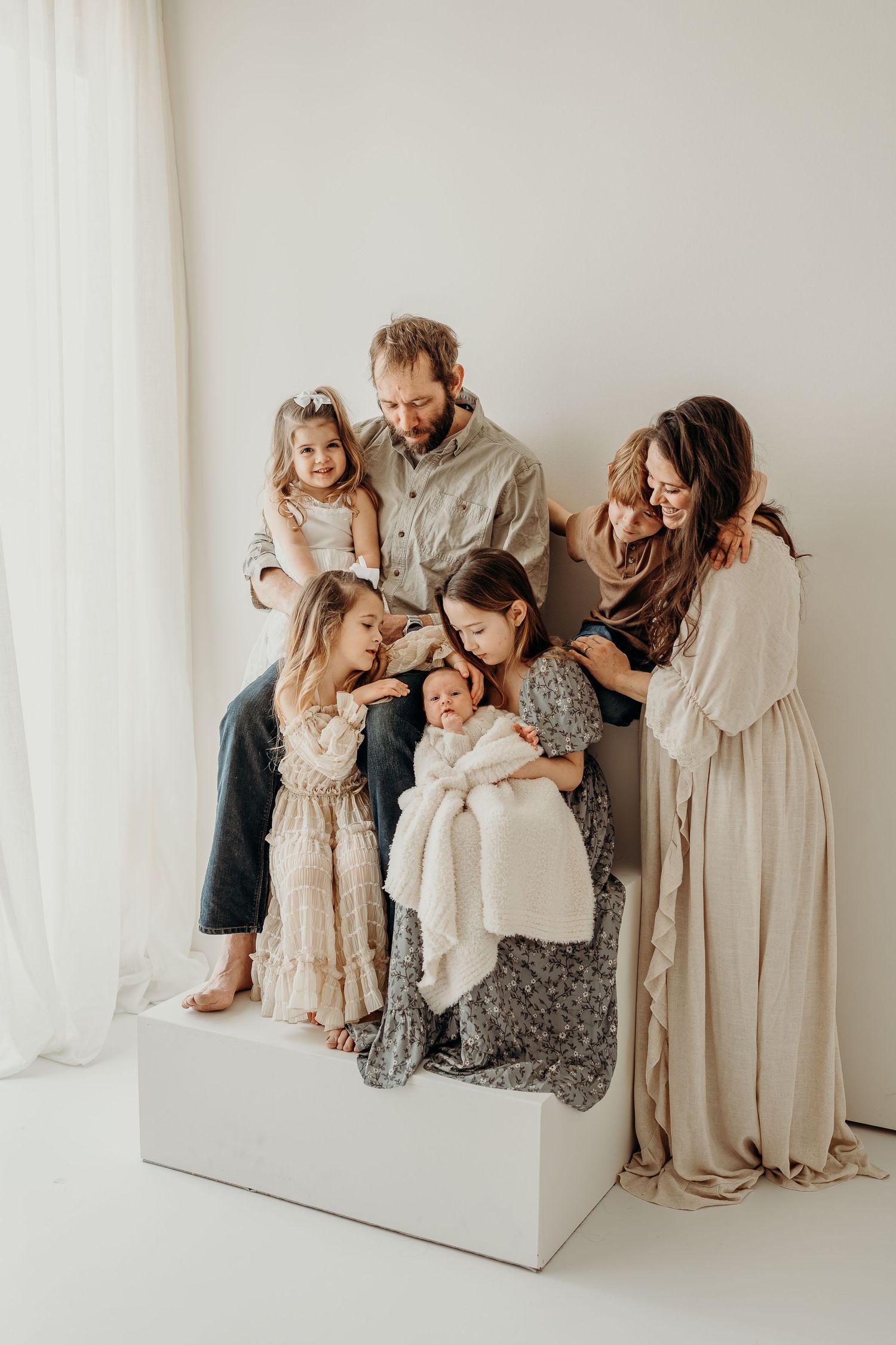 Family in neutral tones poses together against white backdrop in connected lifestyle photo series.