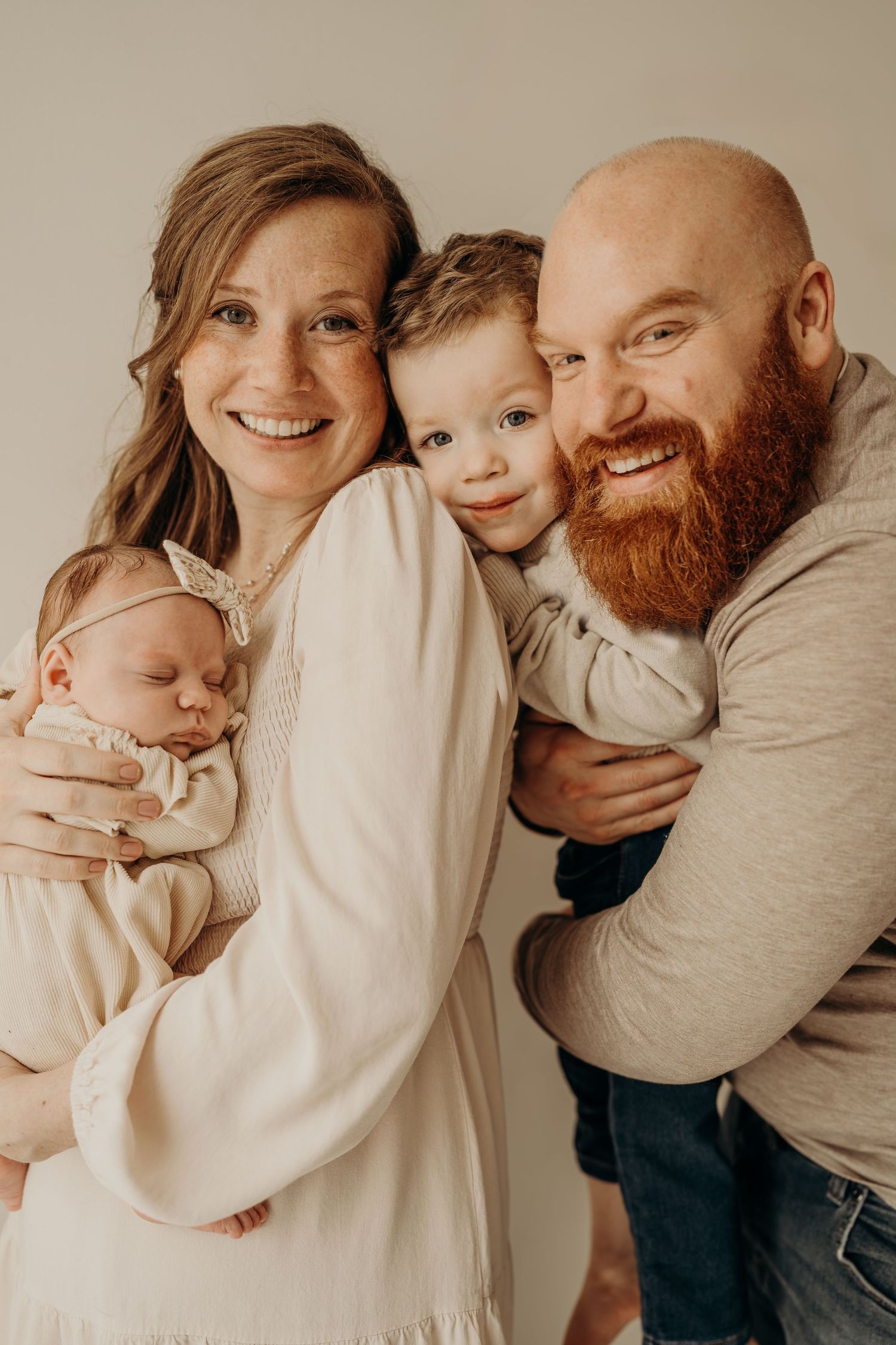 A family portrait in warm tones showing parents with their two young children against a neutral background.