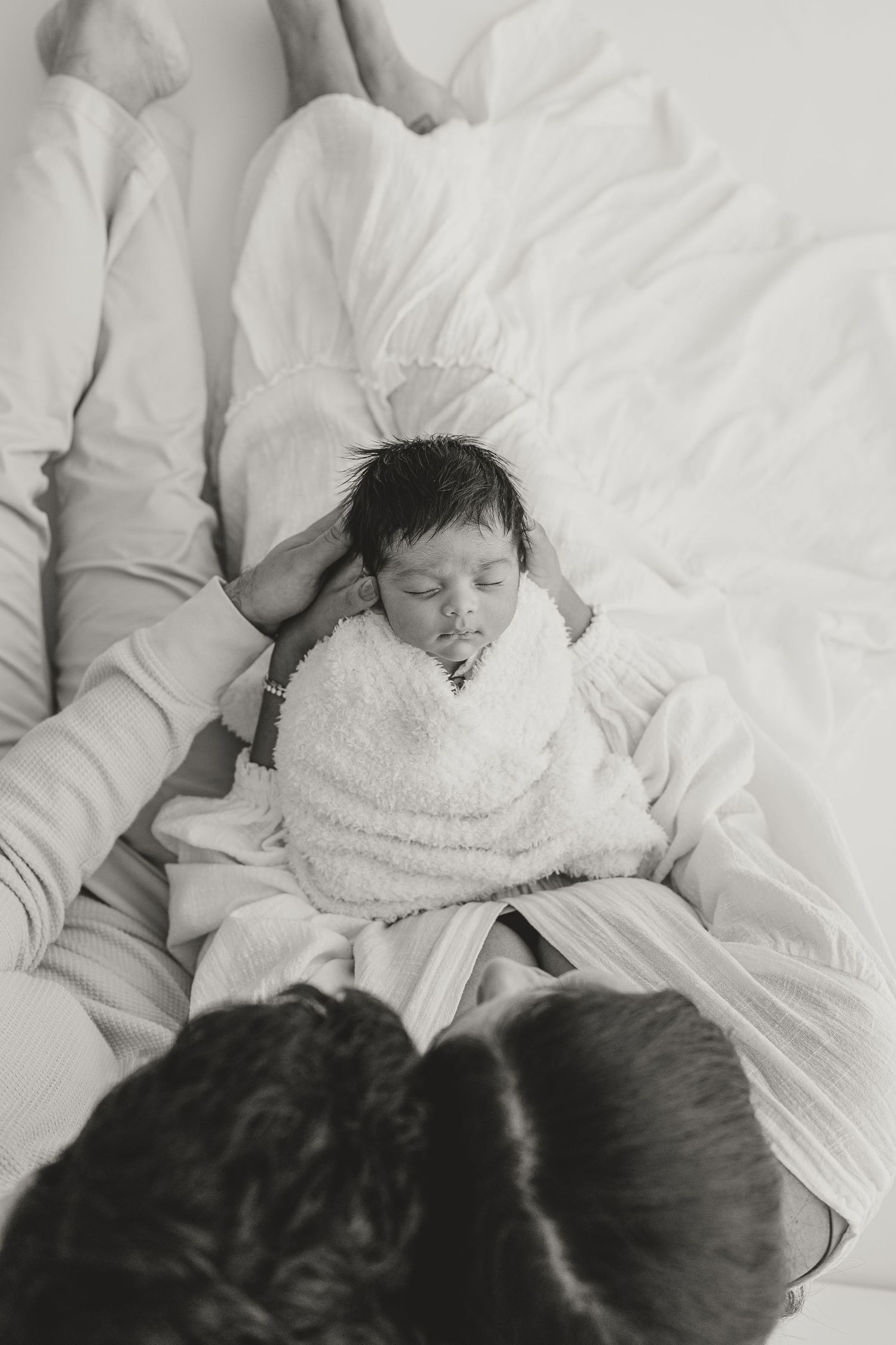 Black and white photo of a newborn baby sleeping peacefully on a bed surrounded by family members captured by Blankslate photography