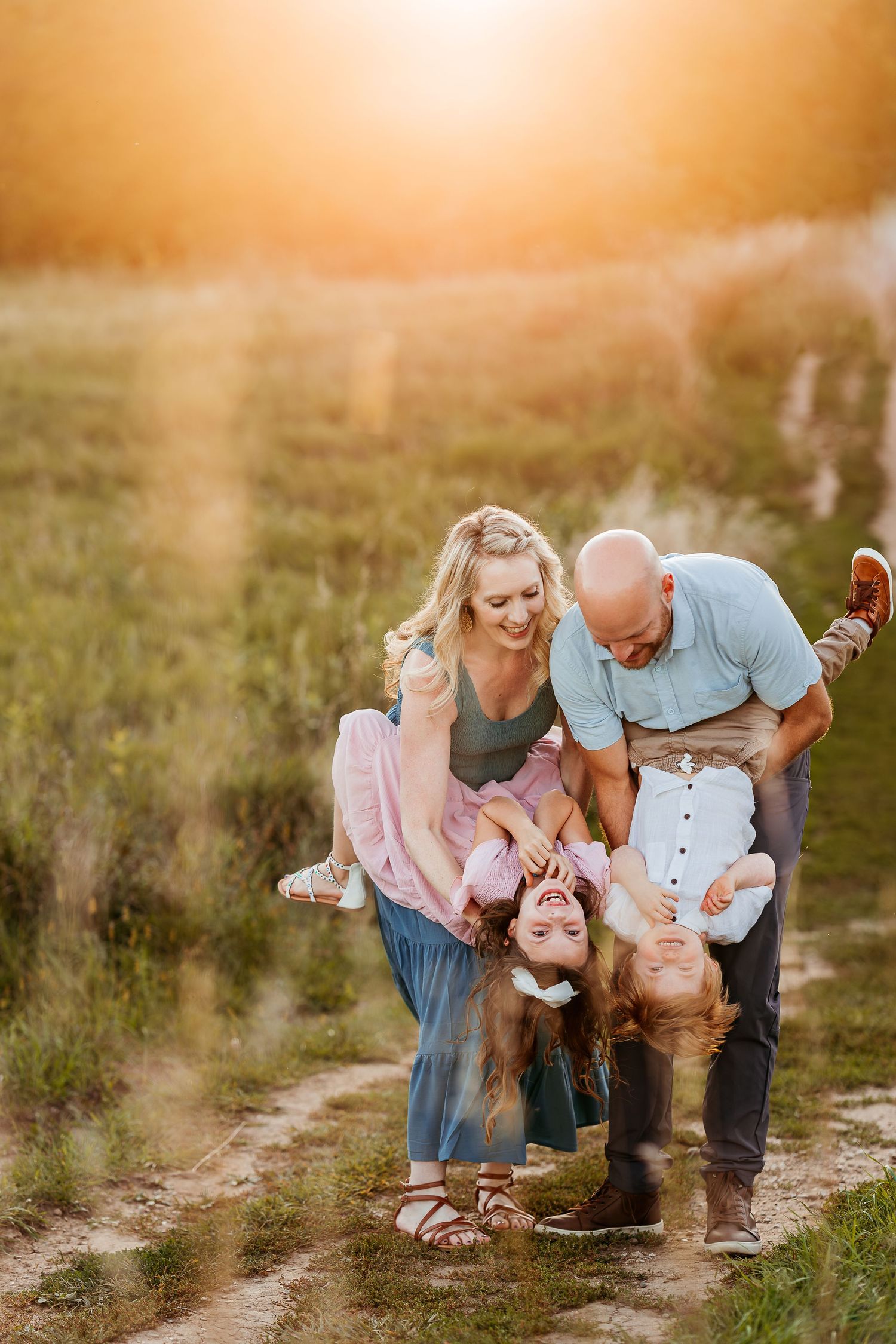 Playful family moment at sunset in a grassy field with children being held upside down.