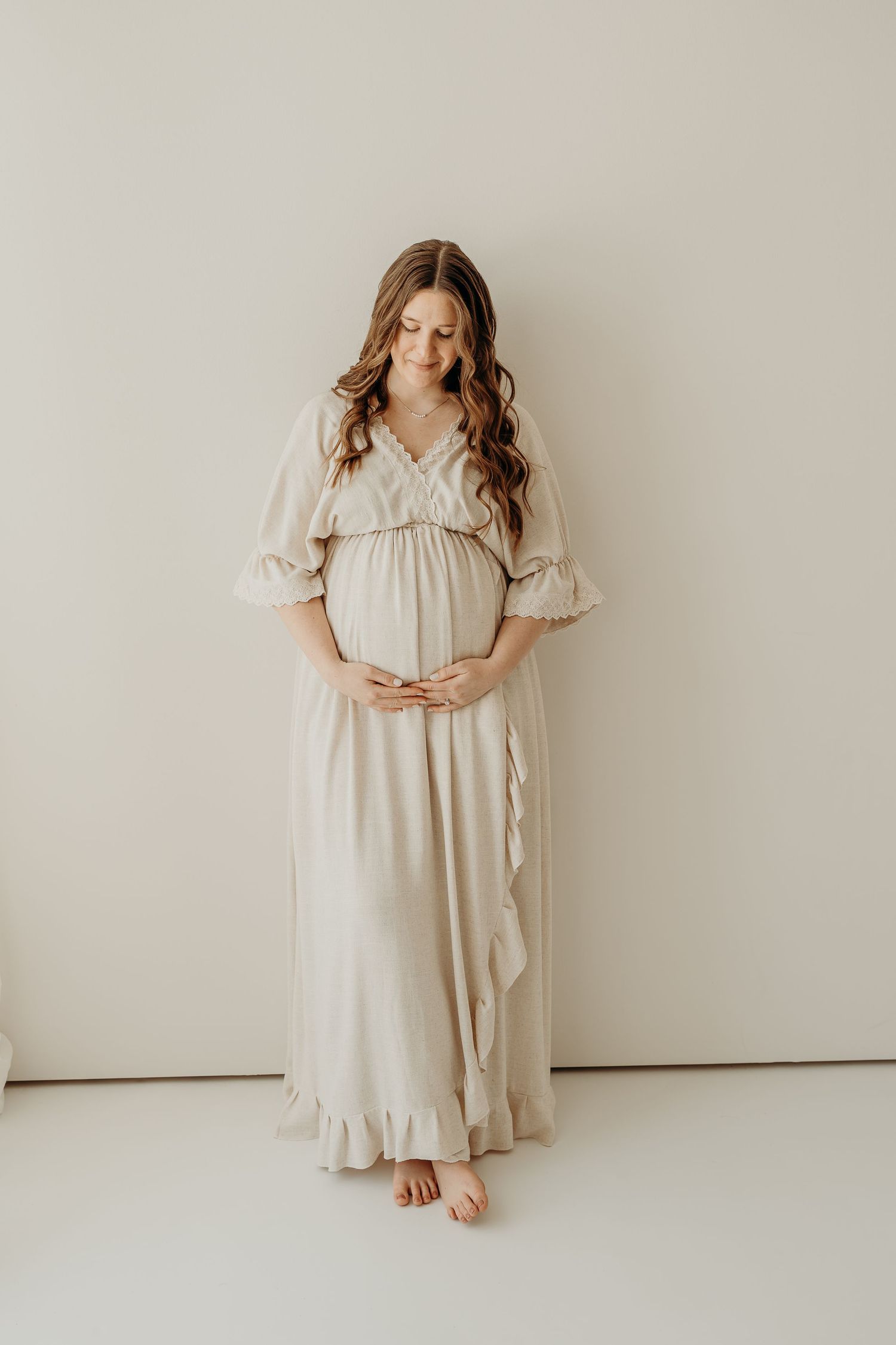 Soft and feminine maternity portraits in cream-colored ruffled dress against white backdrop.