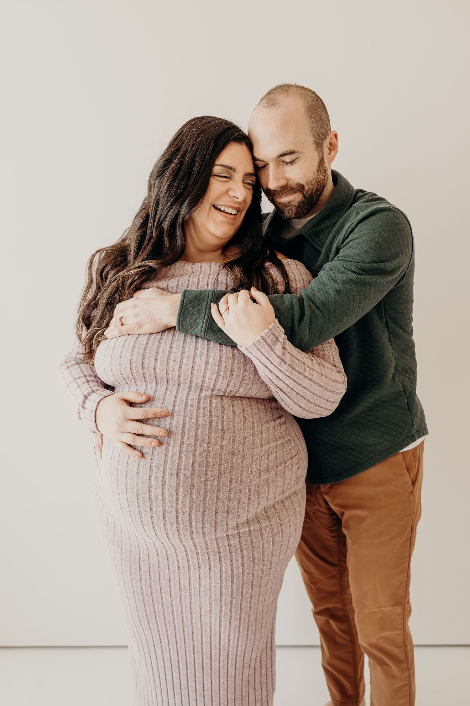 A couple shares a tender moment together against a white backdrop, wearing cozy sweaters and embracing warmly.