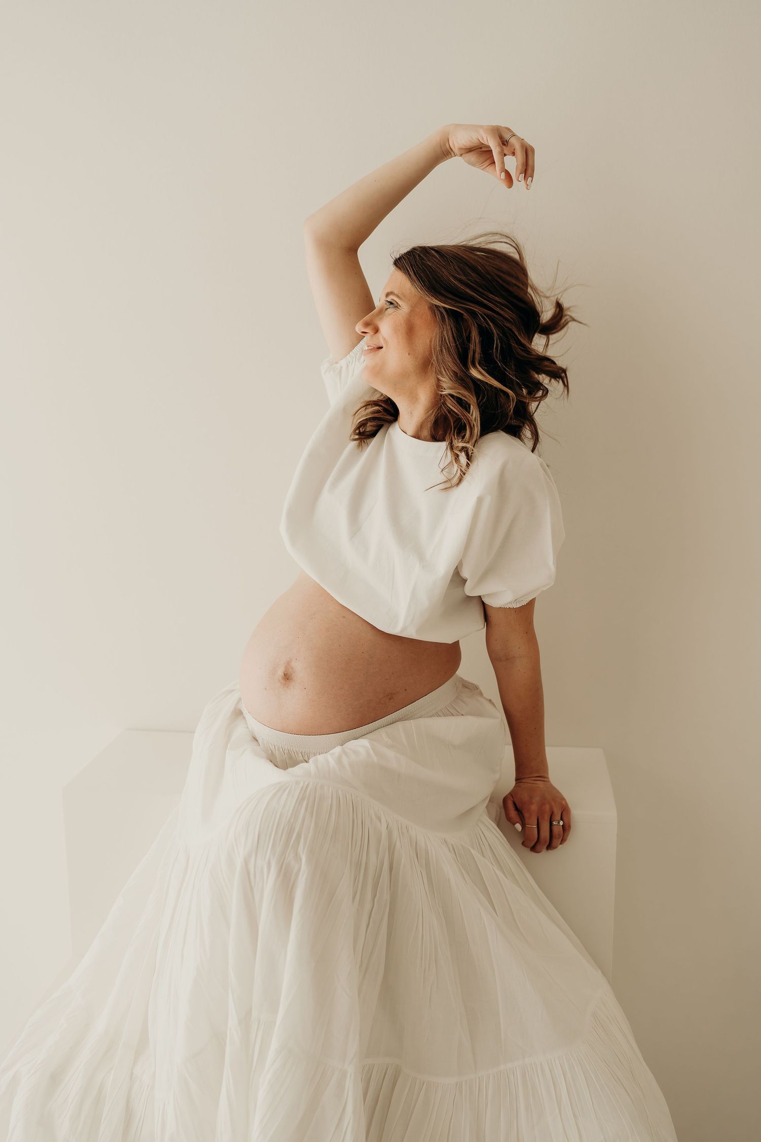 Artistic maternity portrait in white dress showing movement and grace.