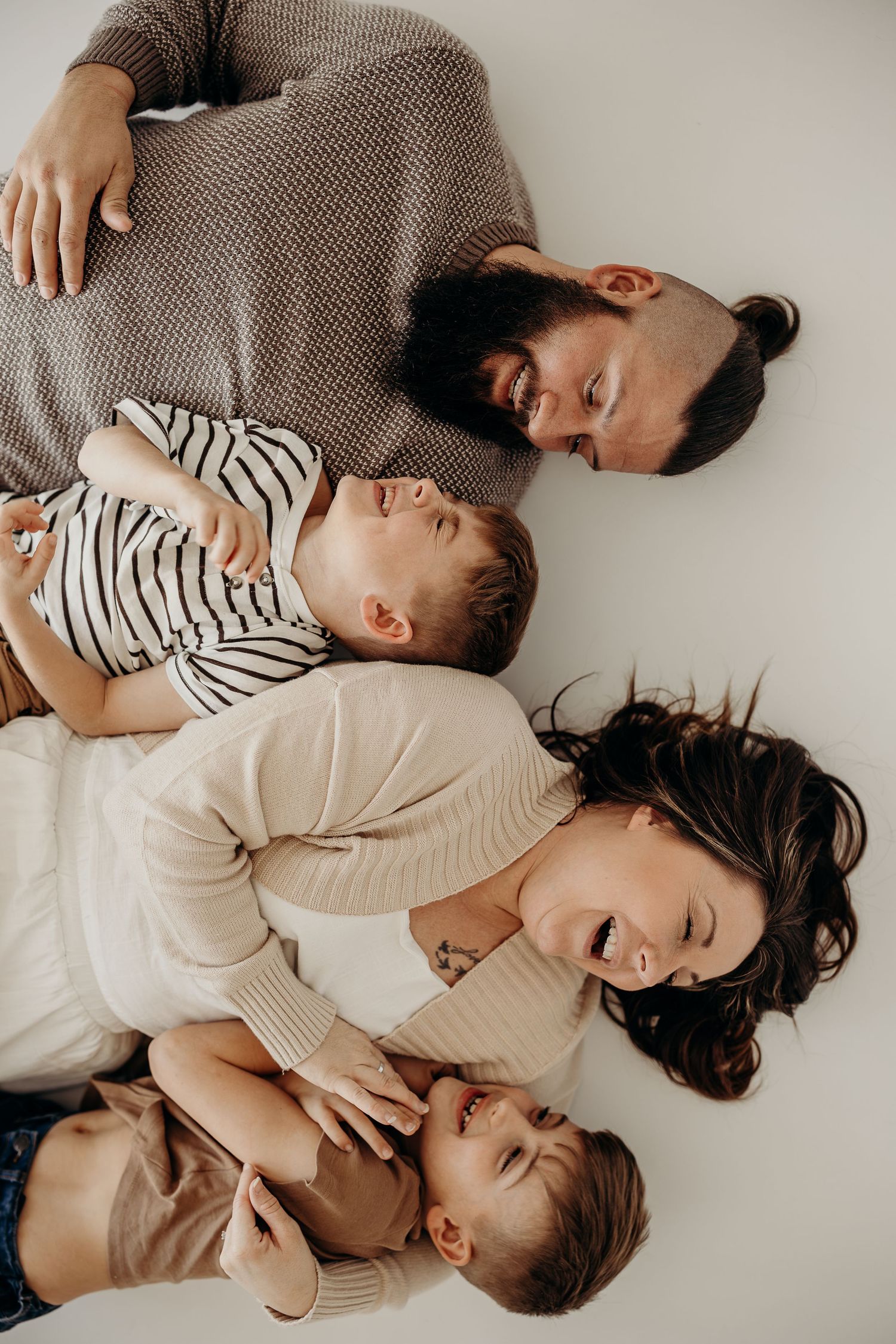 Family lying on floor together in neutral sweaters creating intimate lifestyle portrait.