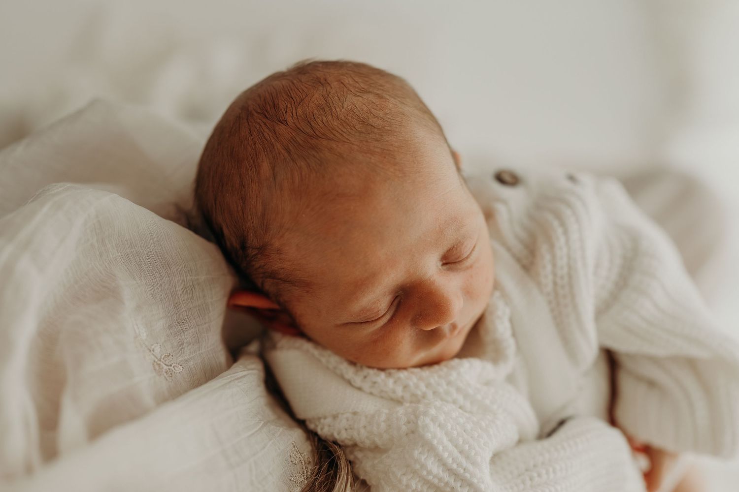 Peaceful newborn baby sleeping wrapped in soft white knit blanket, close-up portrait of serene infant.