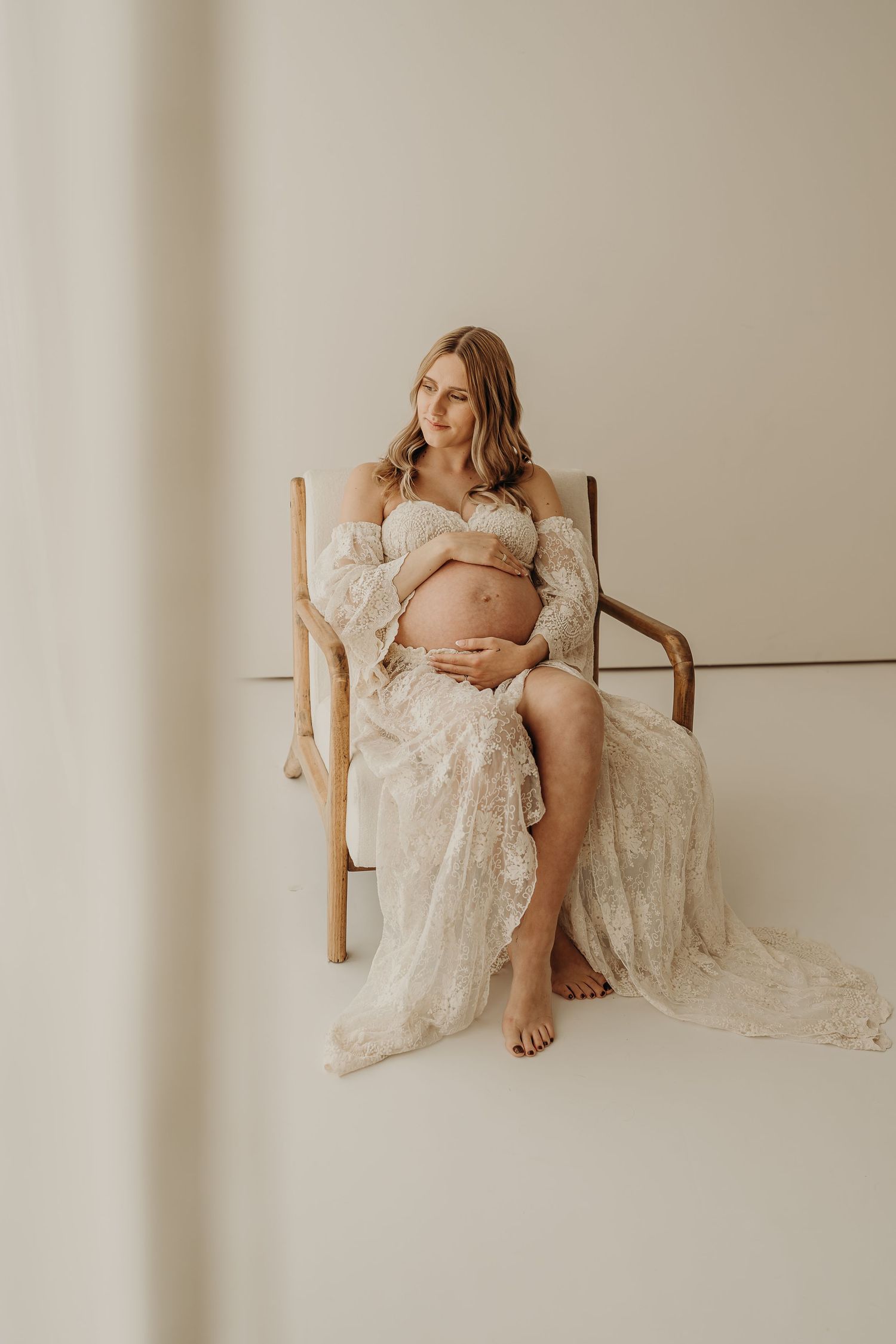 Artistic boudoir photo series showing a figure in white lace reclining on a minimalist wooden bench against neutral wall.