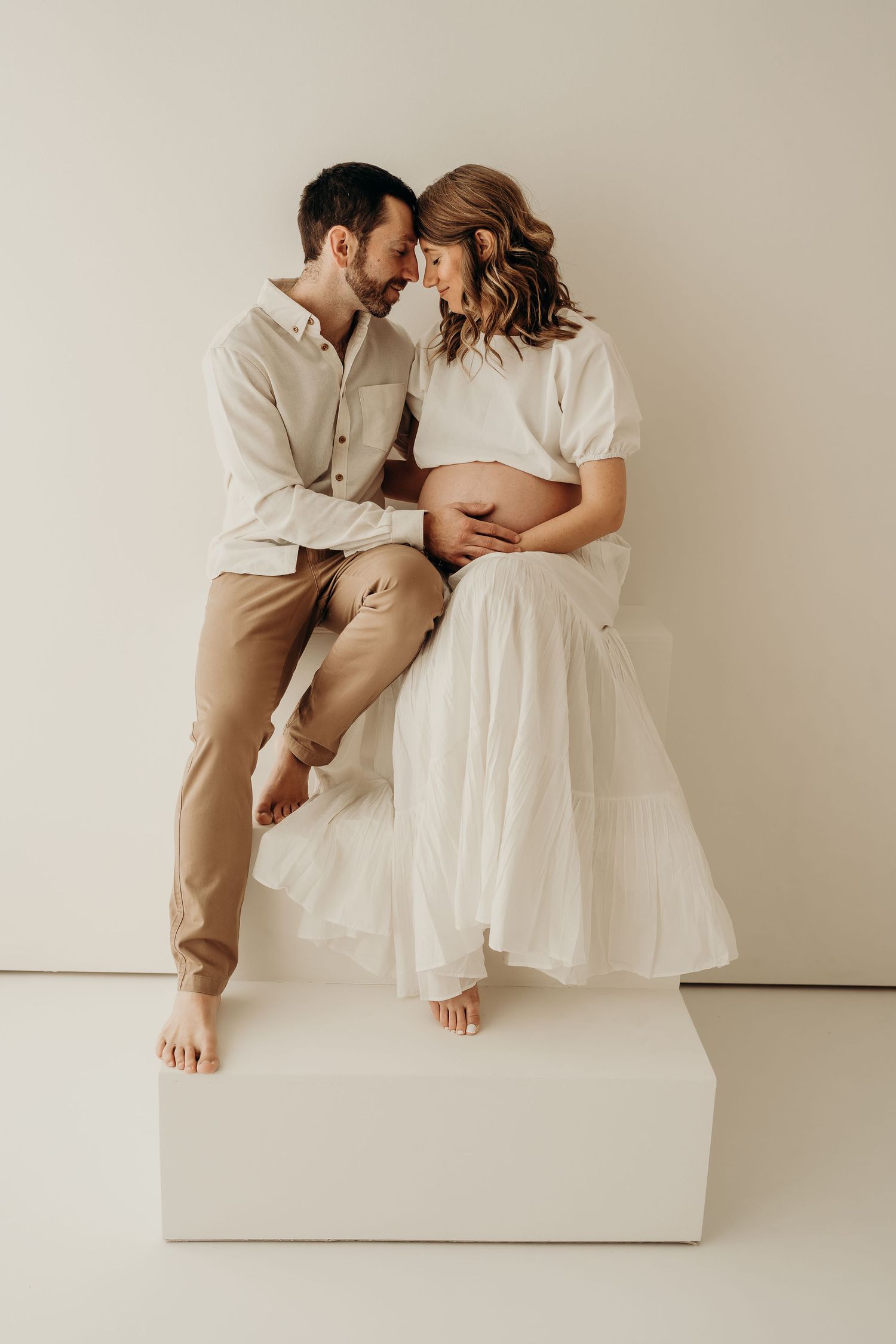 a mom and dad touching foreheads with hands on mom's belly during a studio maternity session, photographed by a maternity photographer