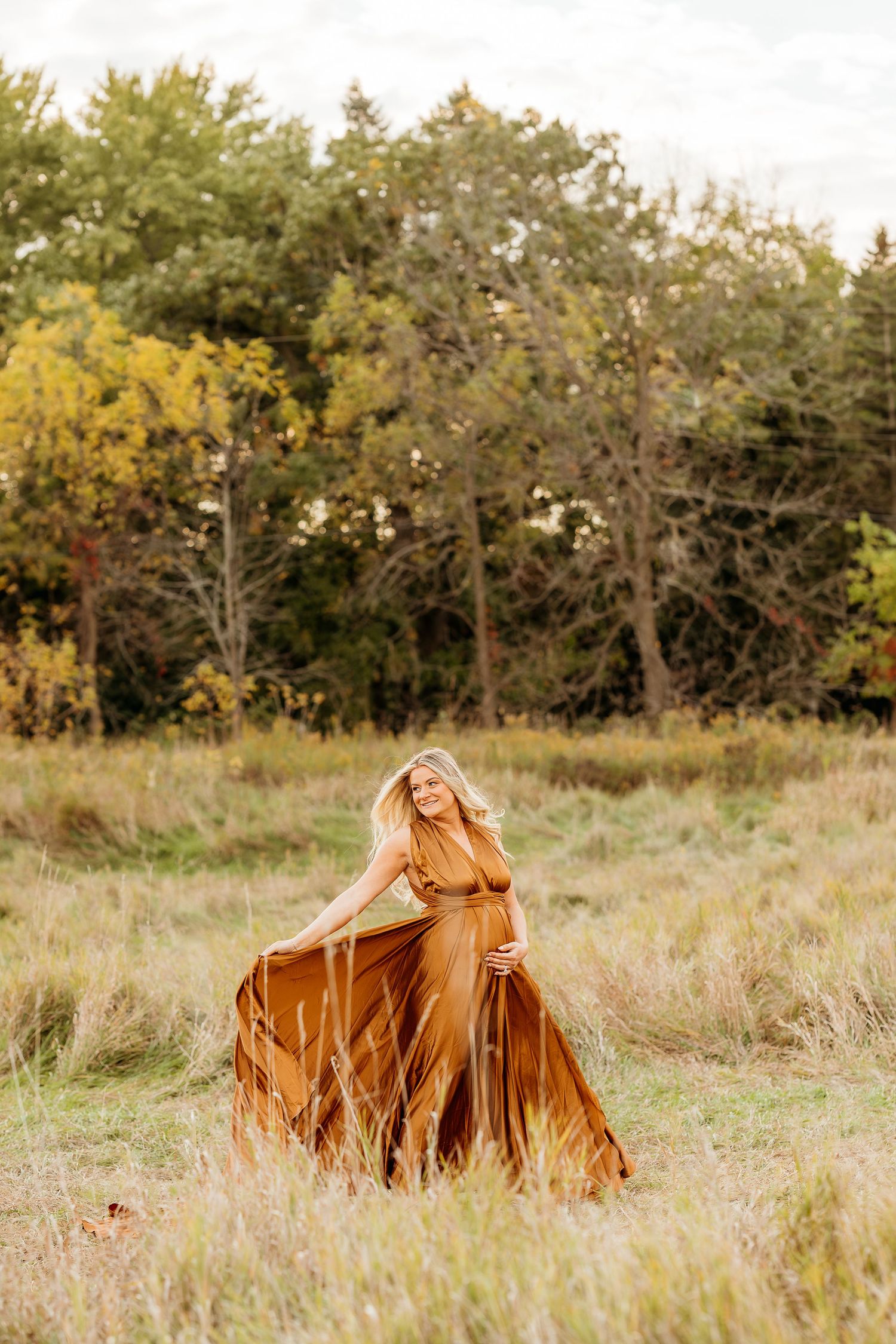 A flowing brown dress twirls gracefully in a sunlit autumn meadow with trees in the background.