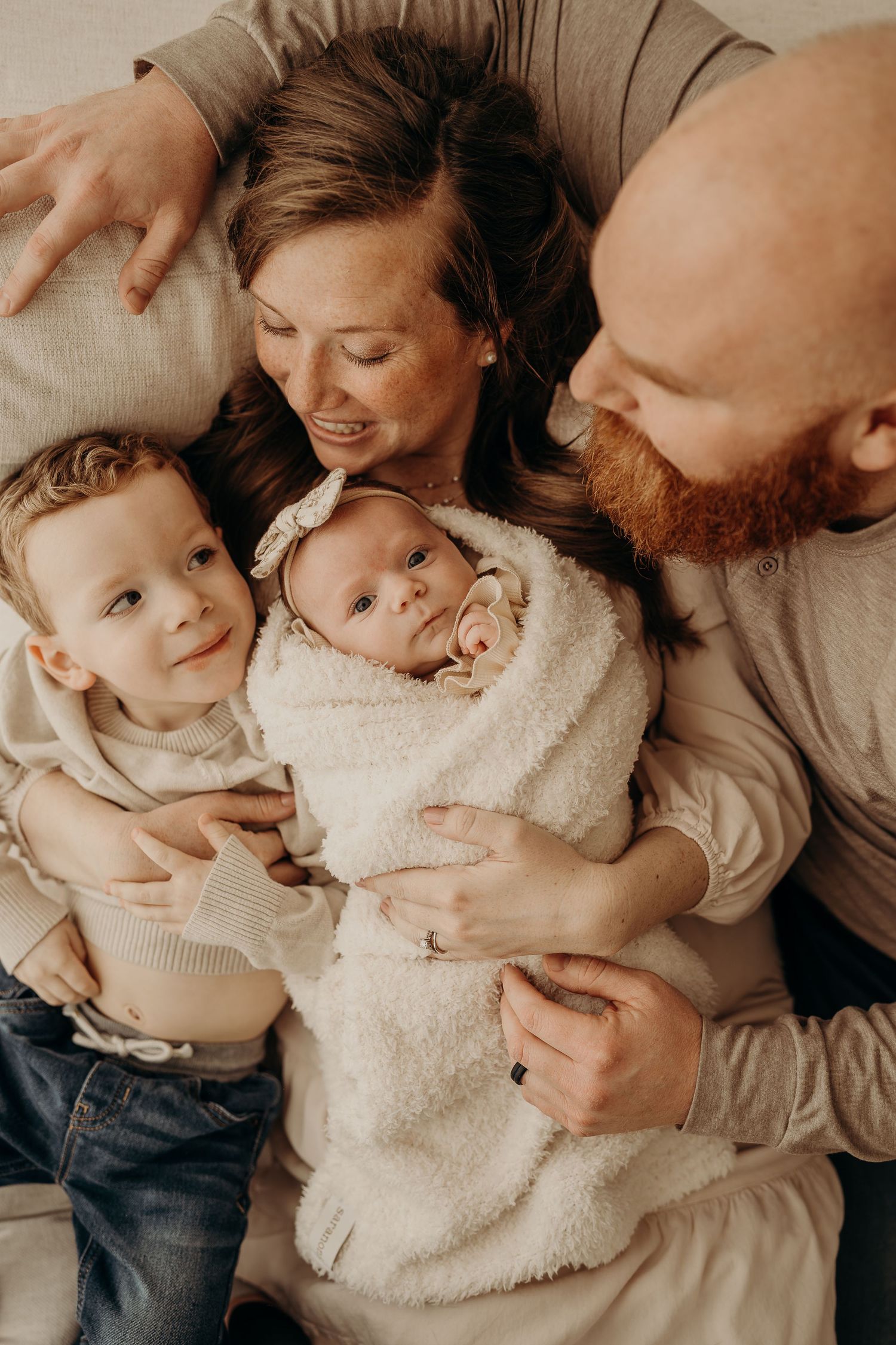Tender family moments captured in warm tones showing loving embraces and cuddles with a baby in cozy white sweaters.