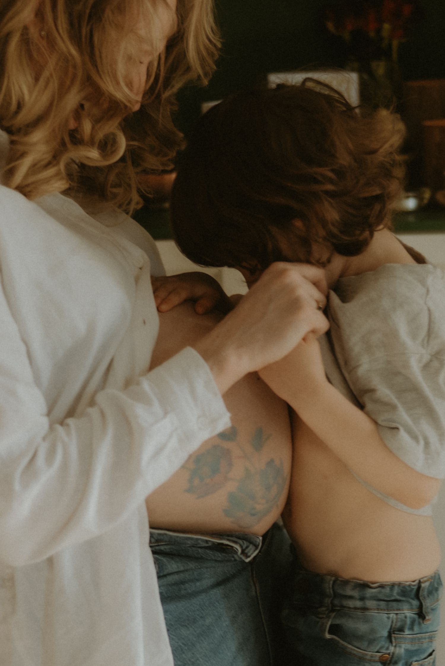 Pregnant woman with floral tattoo helping child with shirt indoors.