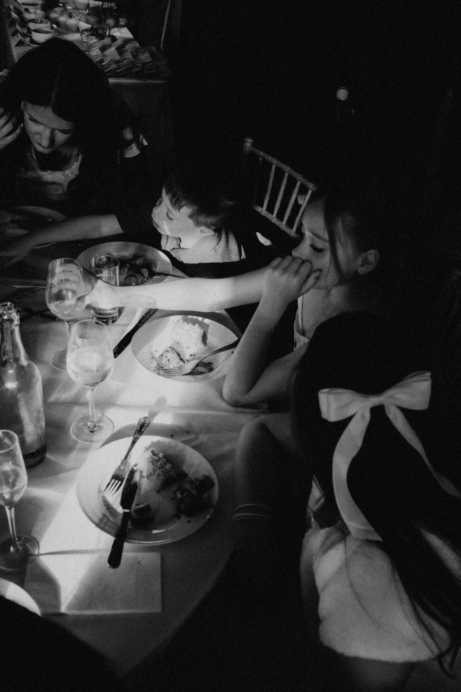 Black and white photo of elegantly dressed women dining at a candlelit table with wine glasses and plates.