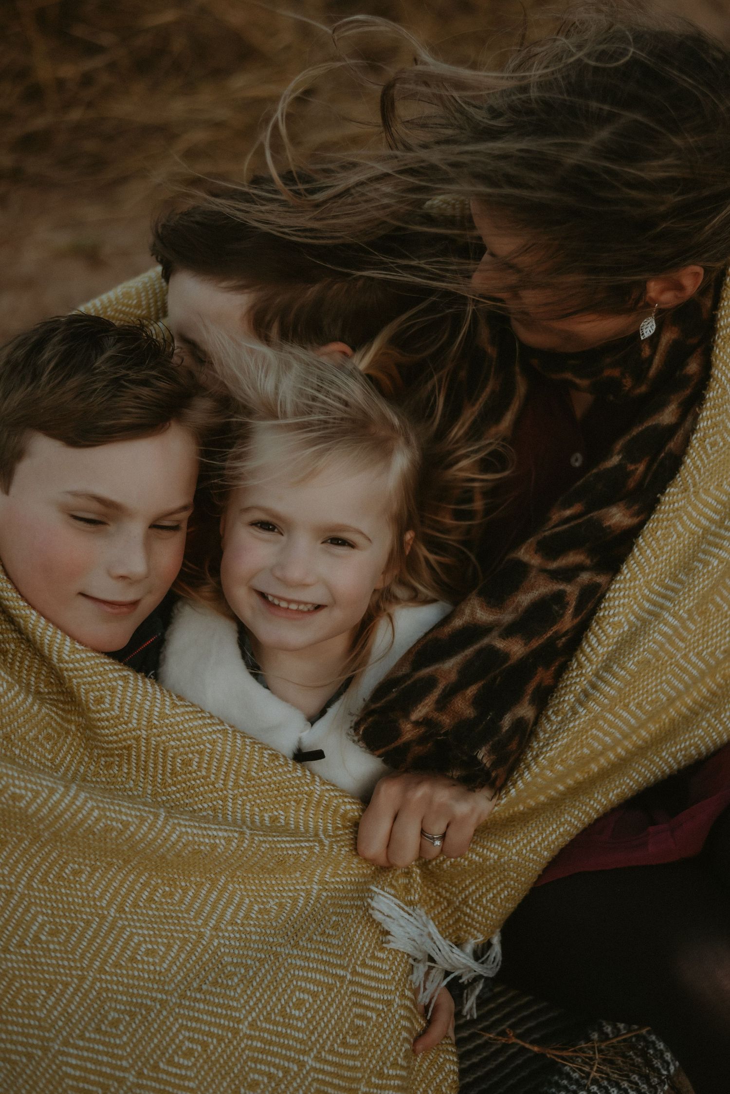 A mother wrapping her two children in a yellow blanket during a windy outdoor session.
