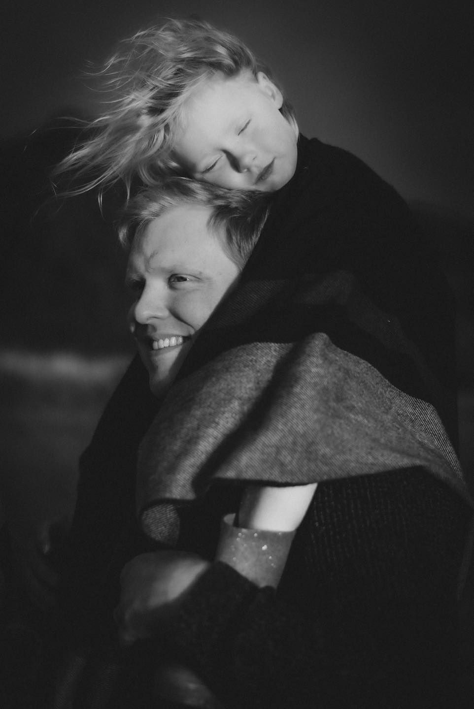 Black and white portrait of a smiling parent giving a child a piggyback ride outdoors.