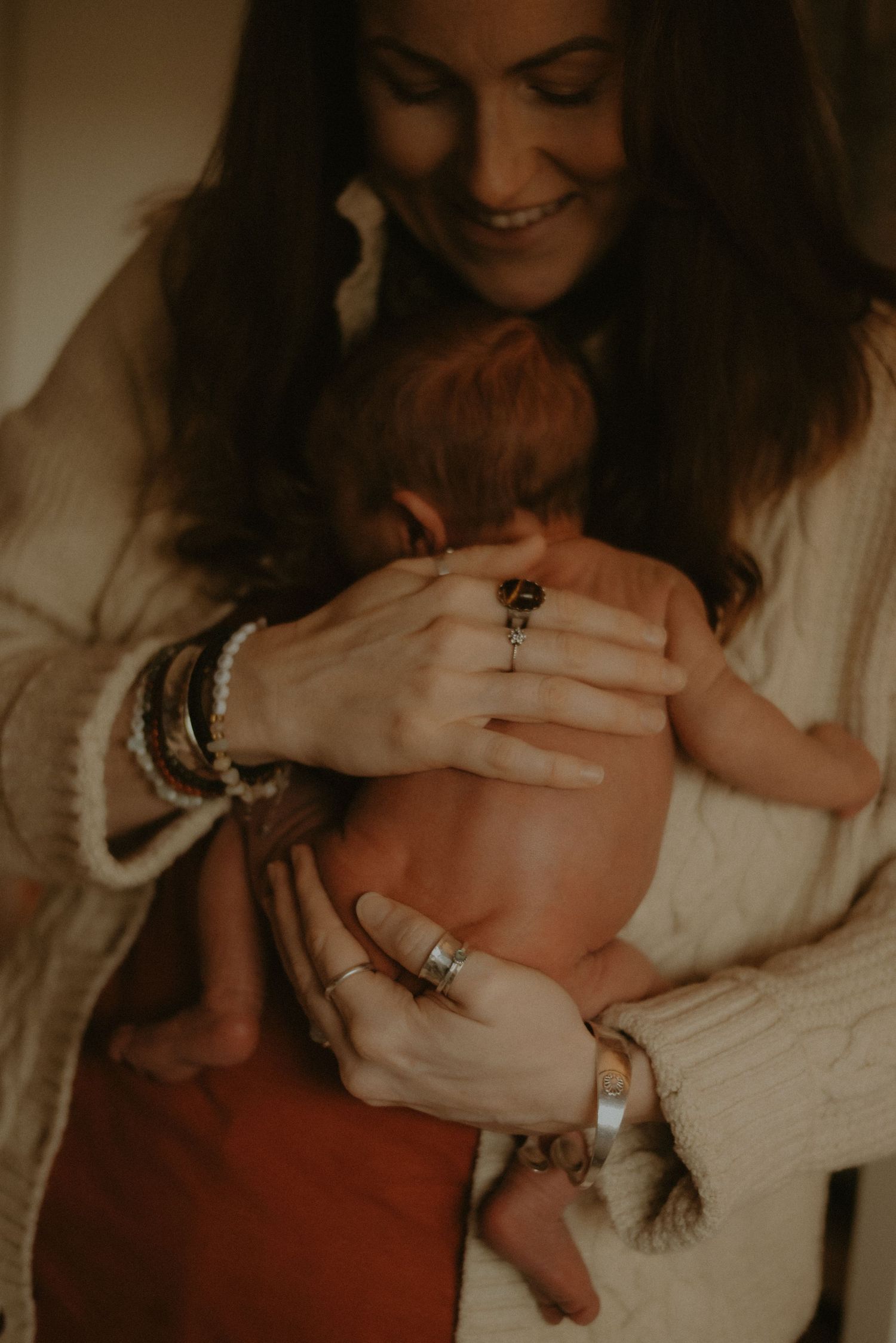 Smiling mother in cream cardigan gently cradles her newborn baby skin-to-skin with tender care.