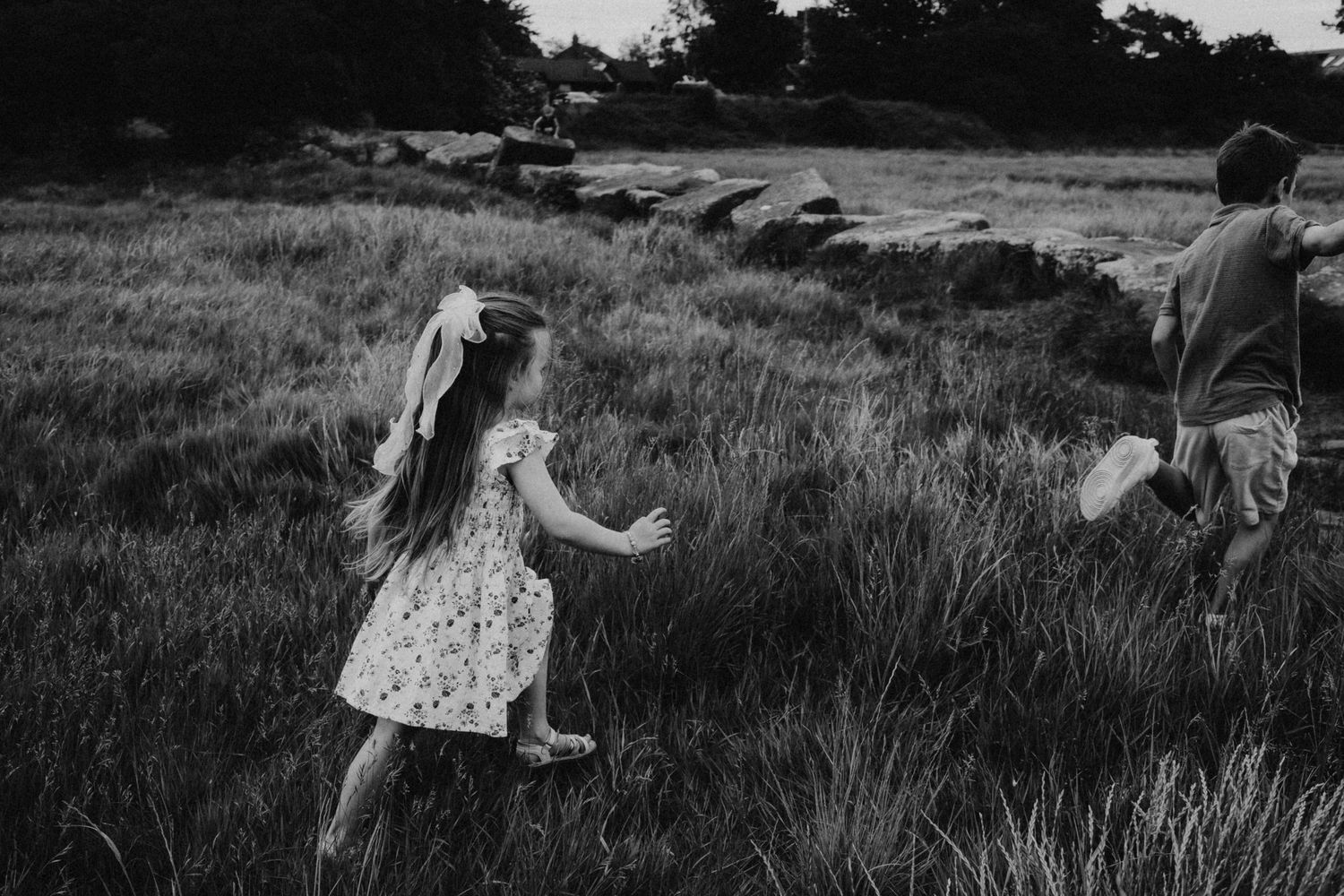 Black and white photo of two children running through a grassy field near a stone wall.