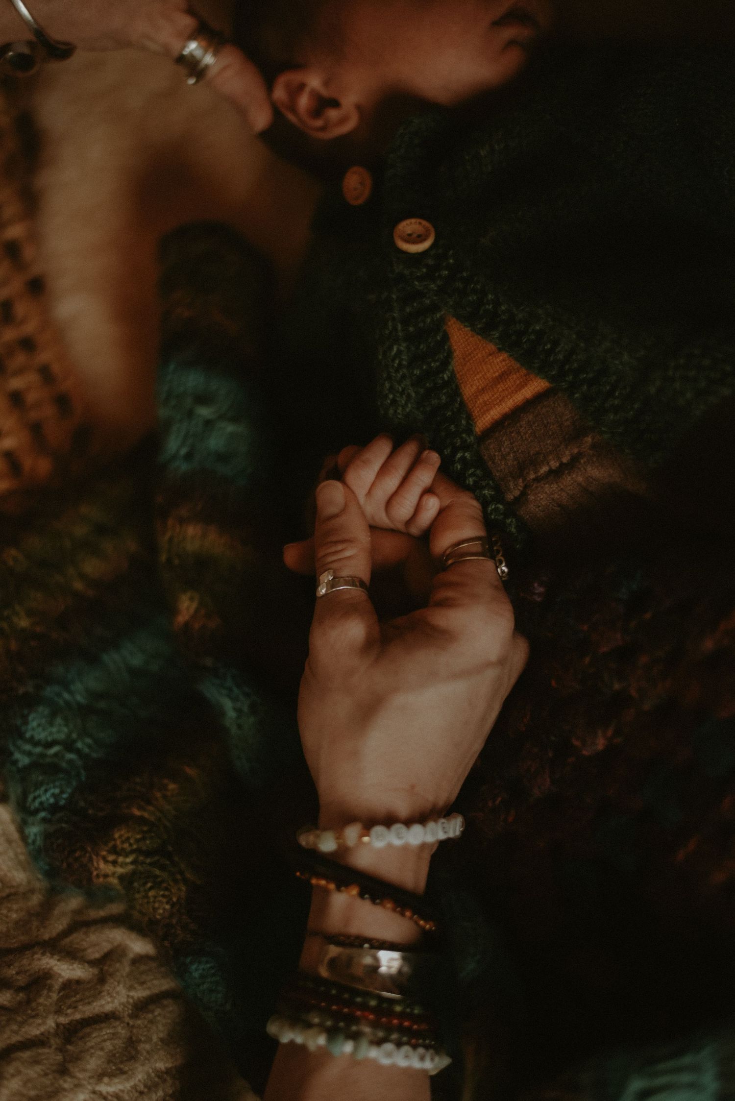 Close-up of a newborn baby grasping an adult's hand adorned with bracelets and rings.