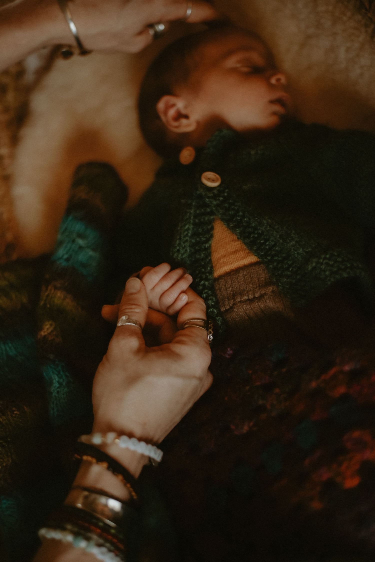 Parent holding newborn baby hand while infant sleeps in knit cardigan.