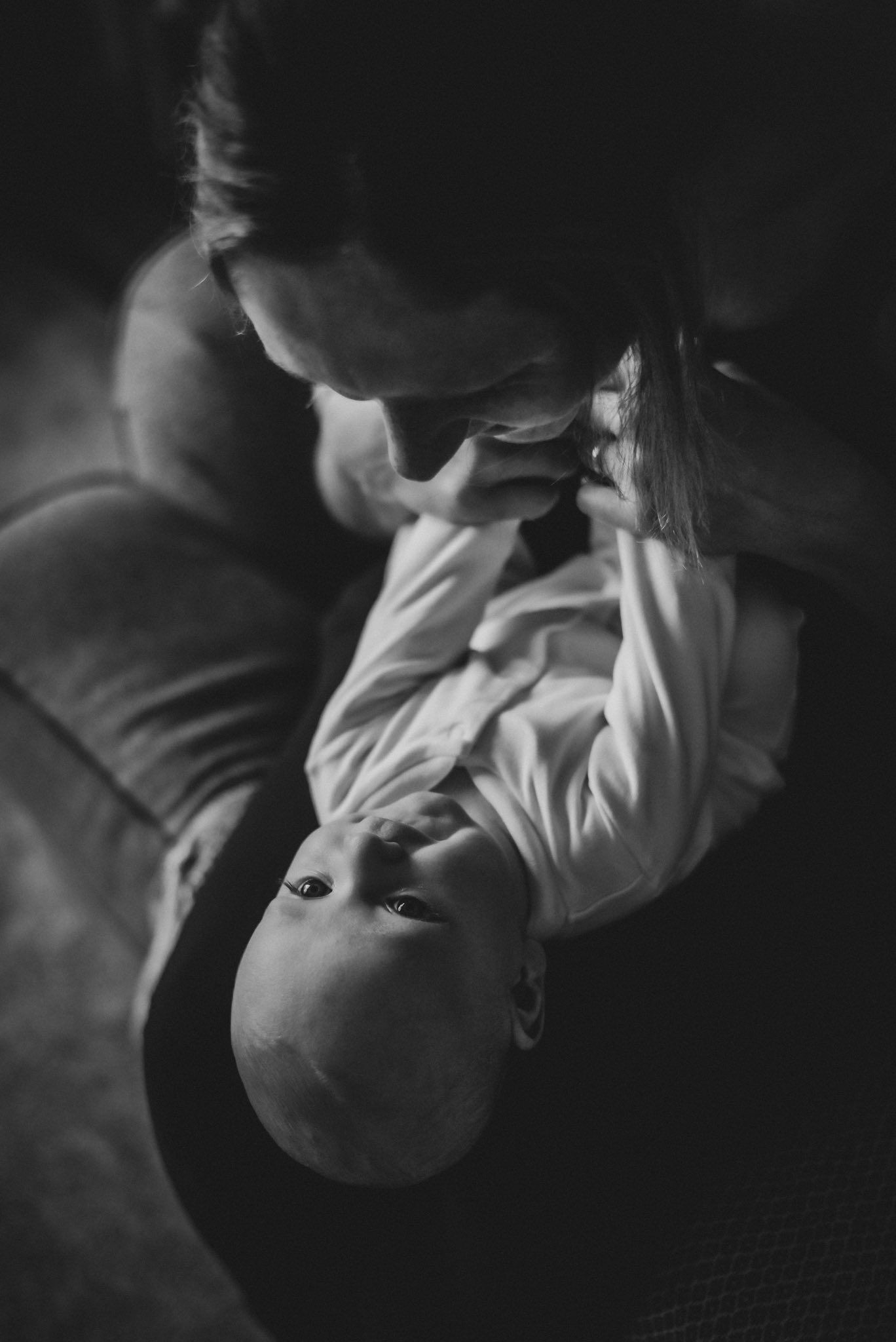 Black and white photo of mother tenderly holding and gazing at her newborn baby indoors.