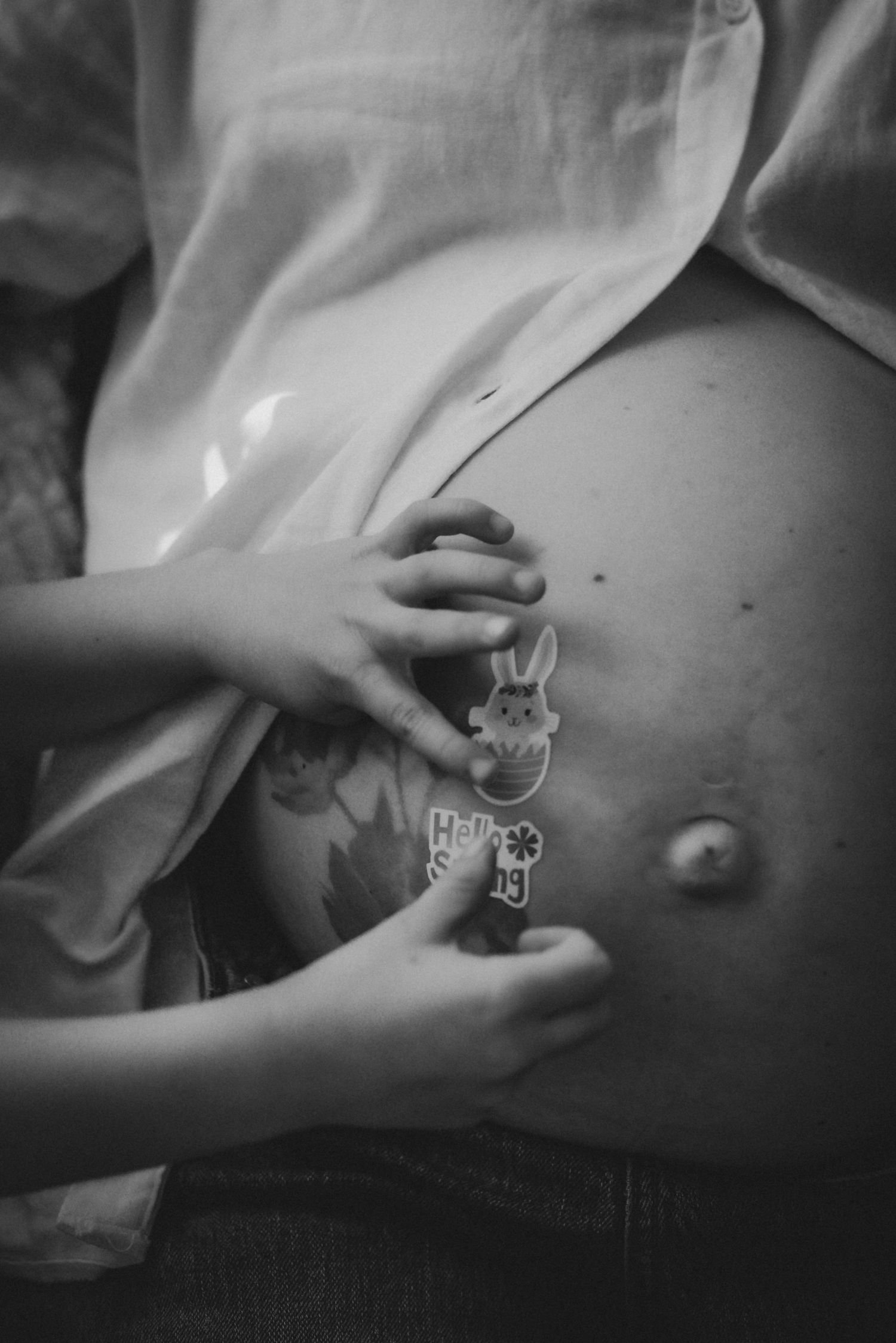 Black and white close-up of pregnant belly with child hand and Easter sticker.