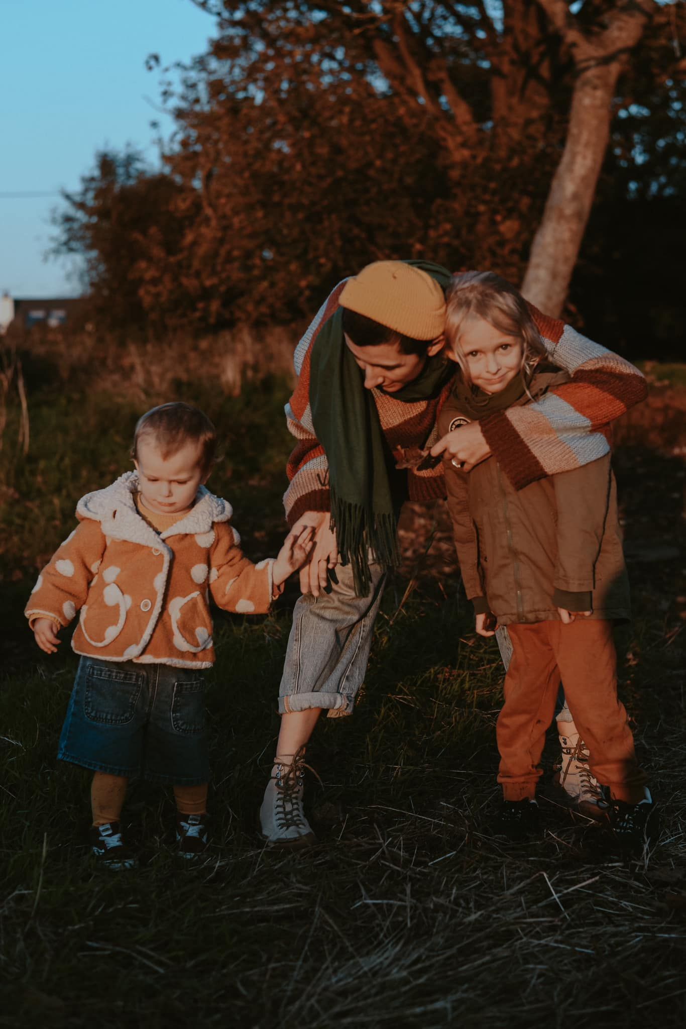 Mother in yellow beret with two young children in autumn field at golden hour dusk.