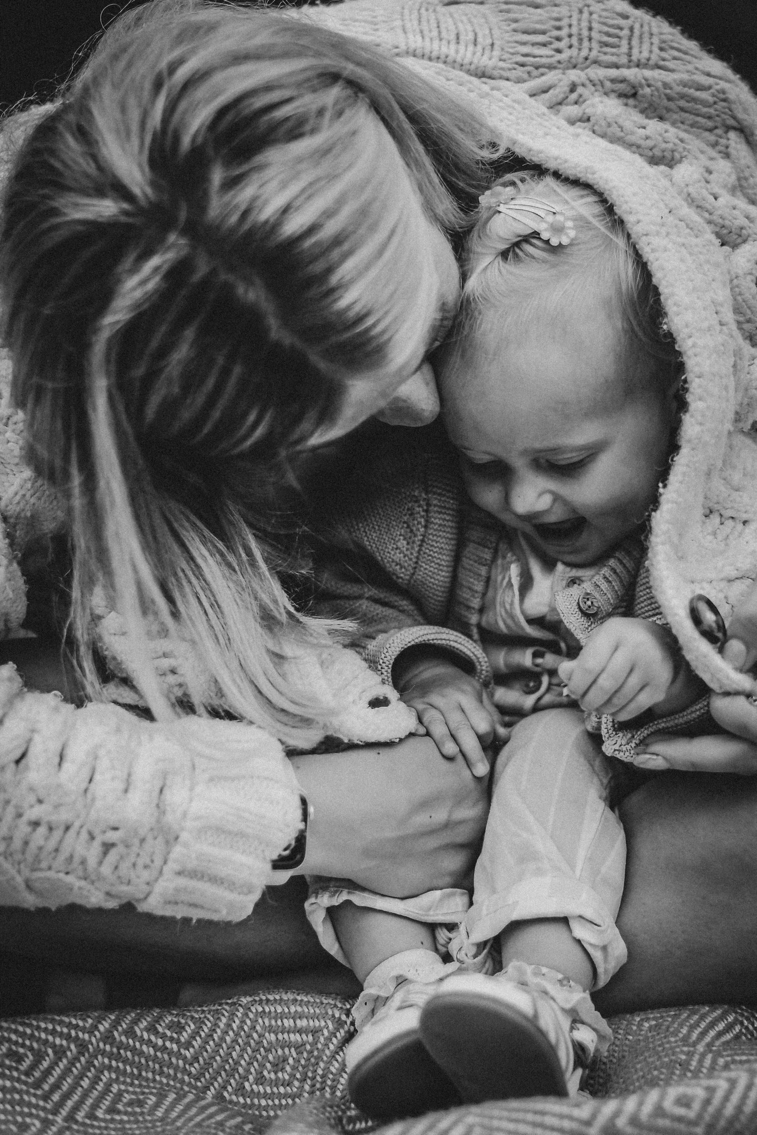Black and white image of a mother nuzzling her laughing baby wrapped in a cozy blanket.
