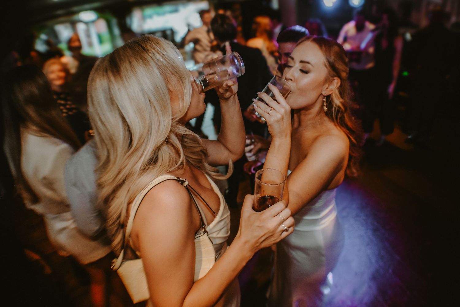 Two women dancing and drinking at a lively nightclub party event.