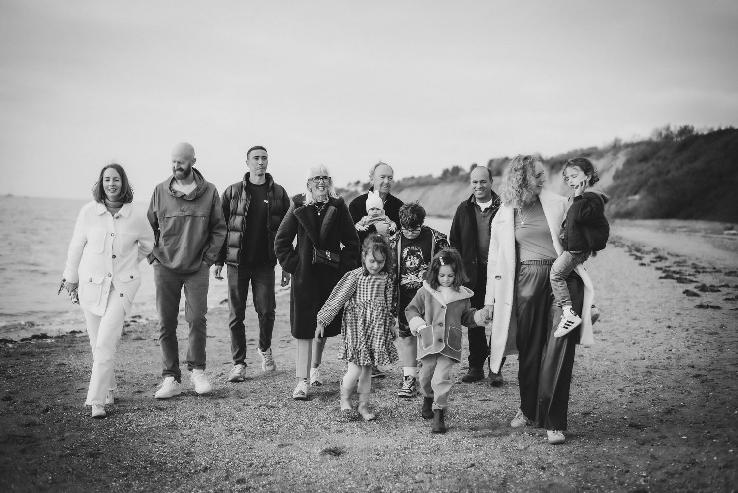 Large family group walking together on a sandy beach in black and white photography.
