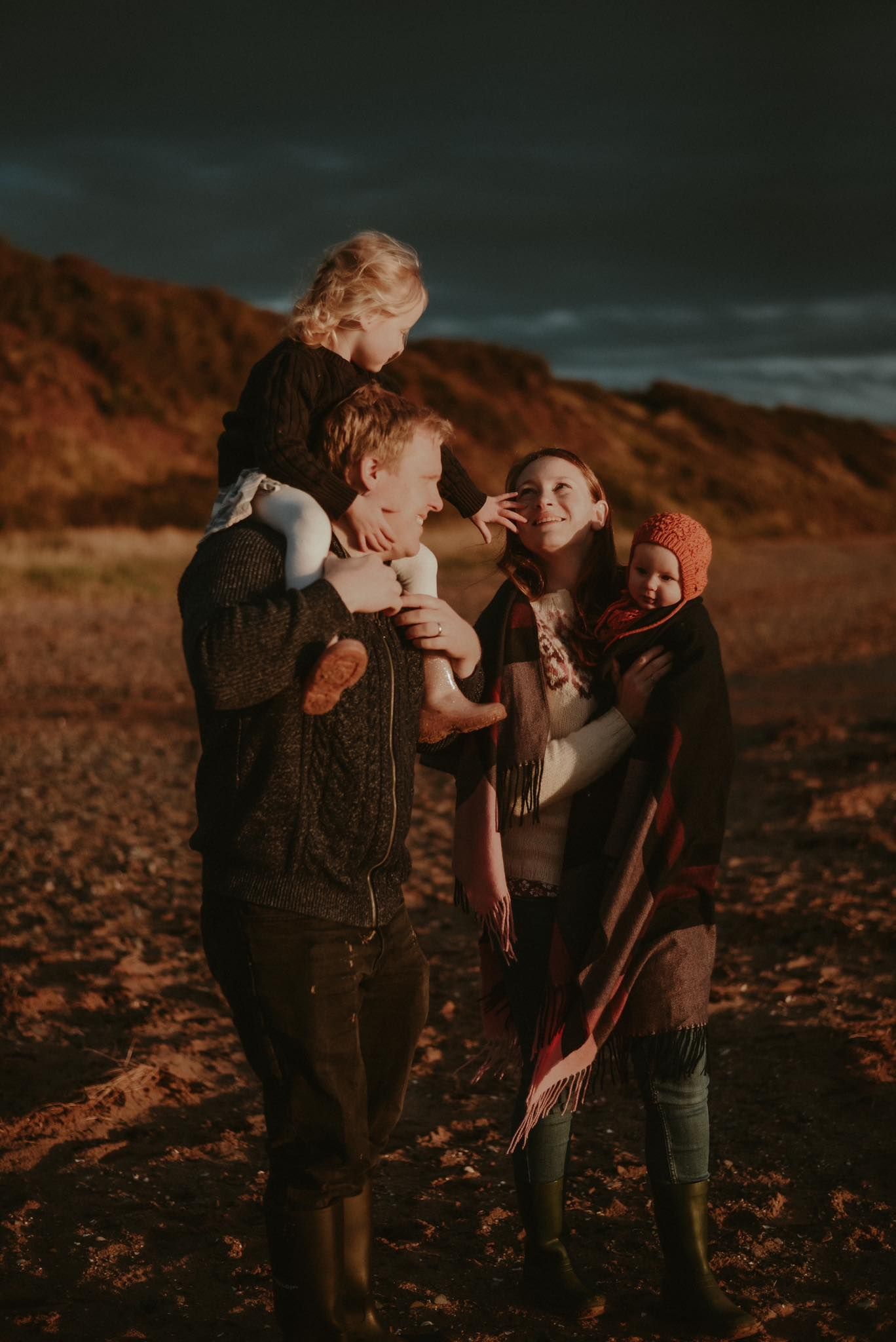 Family of five sharing a warm moment on a beach at dusk, wrapped in cozy autumn clothing.