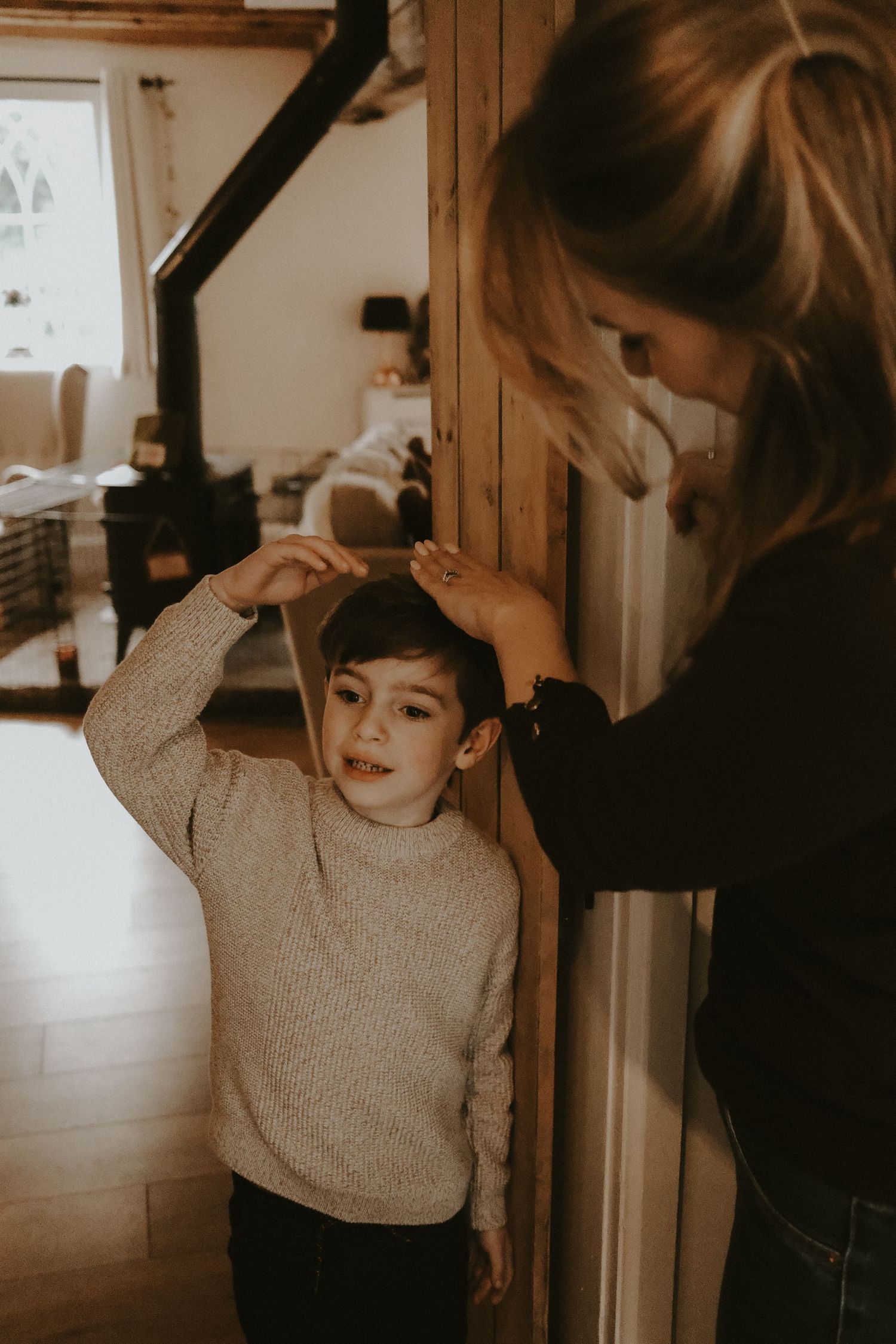 Woman measuring young boy's height against a wooden door frame indoors.