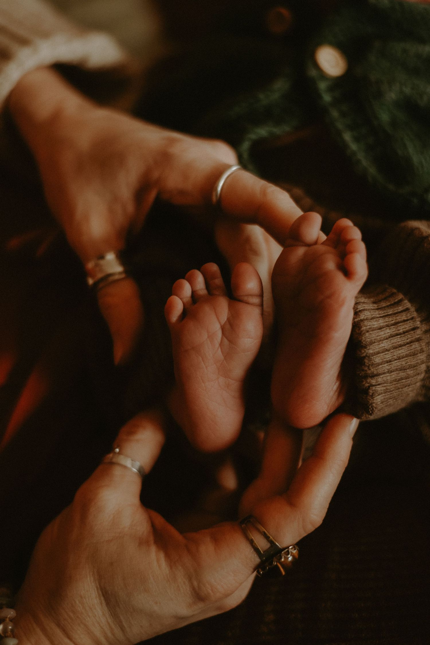 Close-up of parents gently cradling tiny newborn feet in their hands with silver rings.