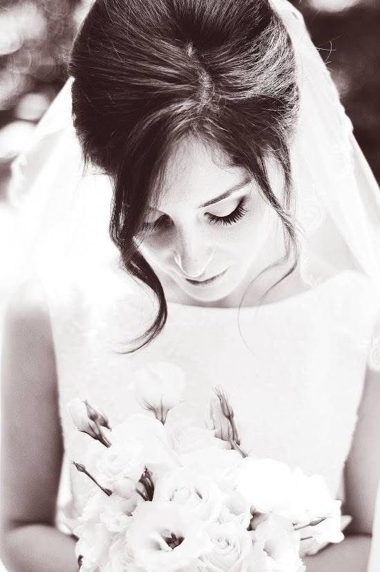 Black and white portrait of a bride in a white dress and veil, looking down at her bouquet of white flowers.