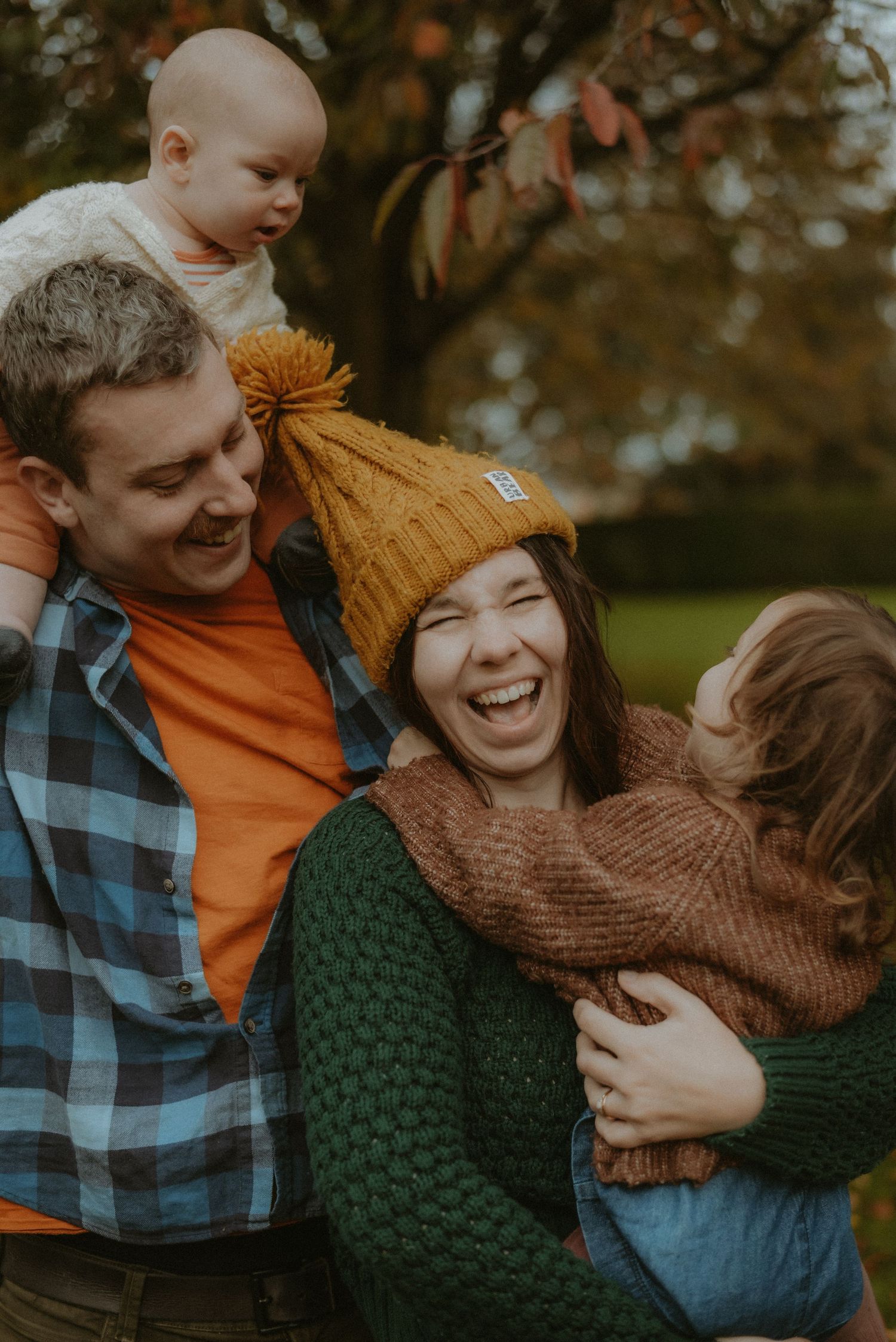 A laughing family of four with two young children enjoying an autumn day in the park.