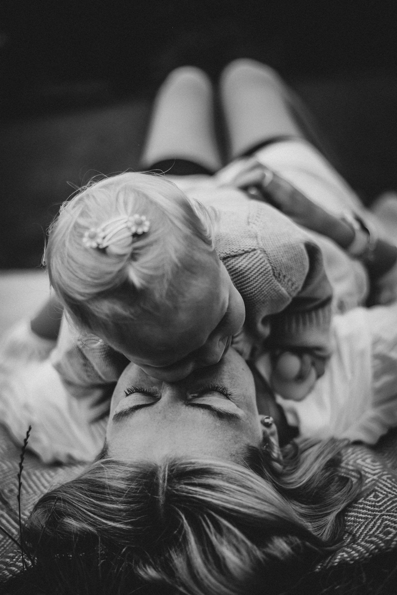 Black and white portrait of mother lying down while her baby girl rests on her face.