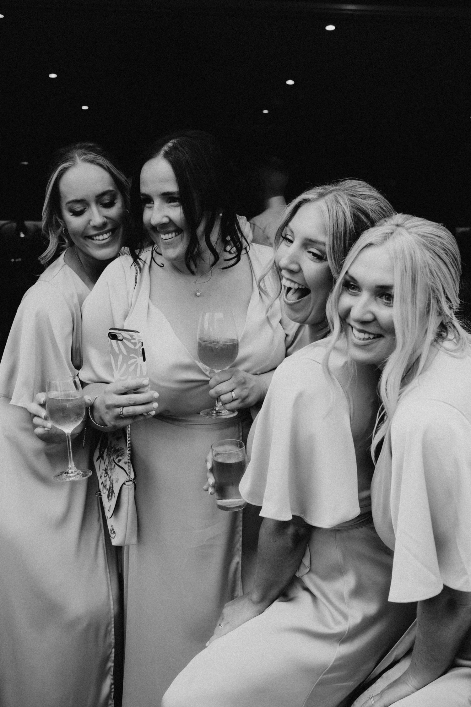 Black and white photo of bridesmaids laughing and holding champagne glasses at a wedding celebration.