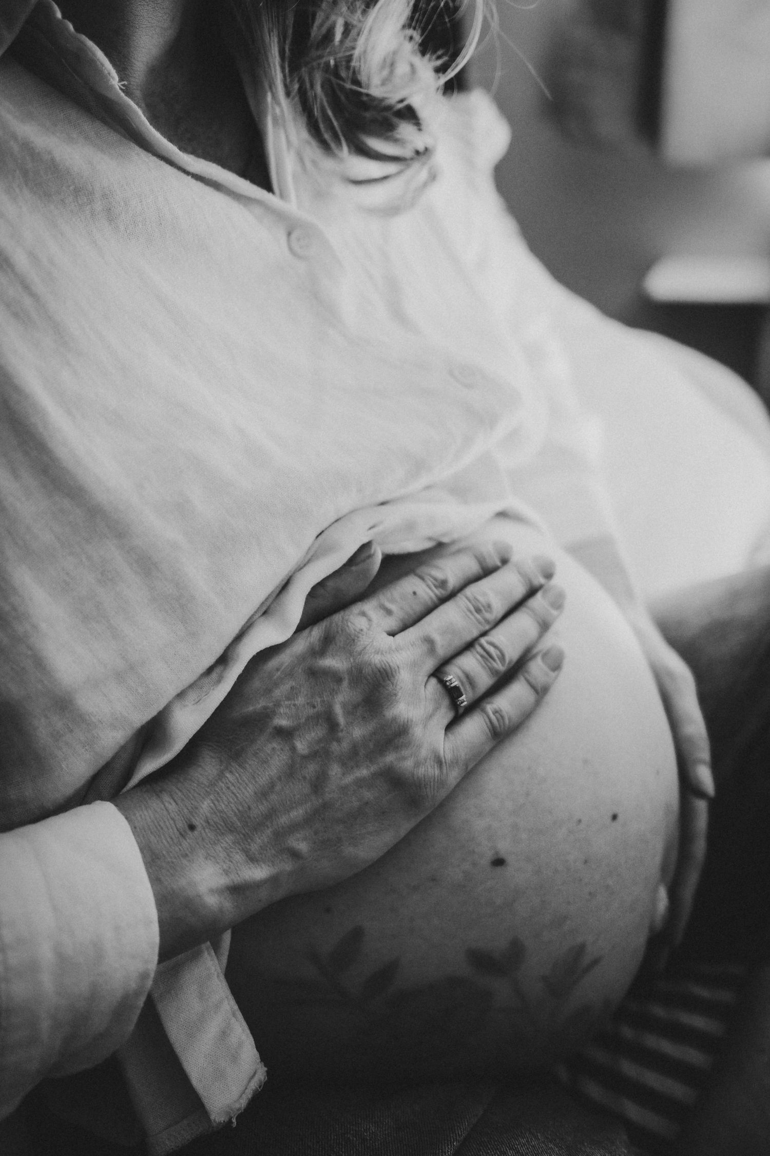 Black and white close-up of hand resting on pregnant belly with visible tattoo.