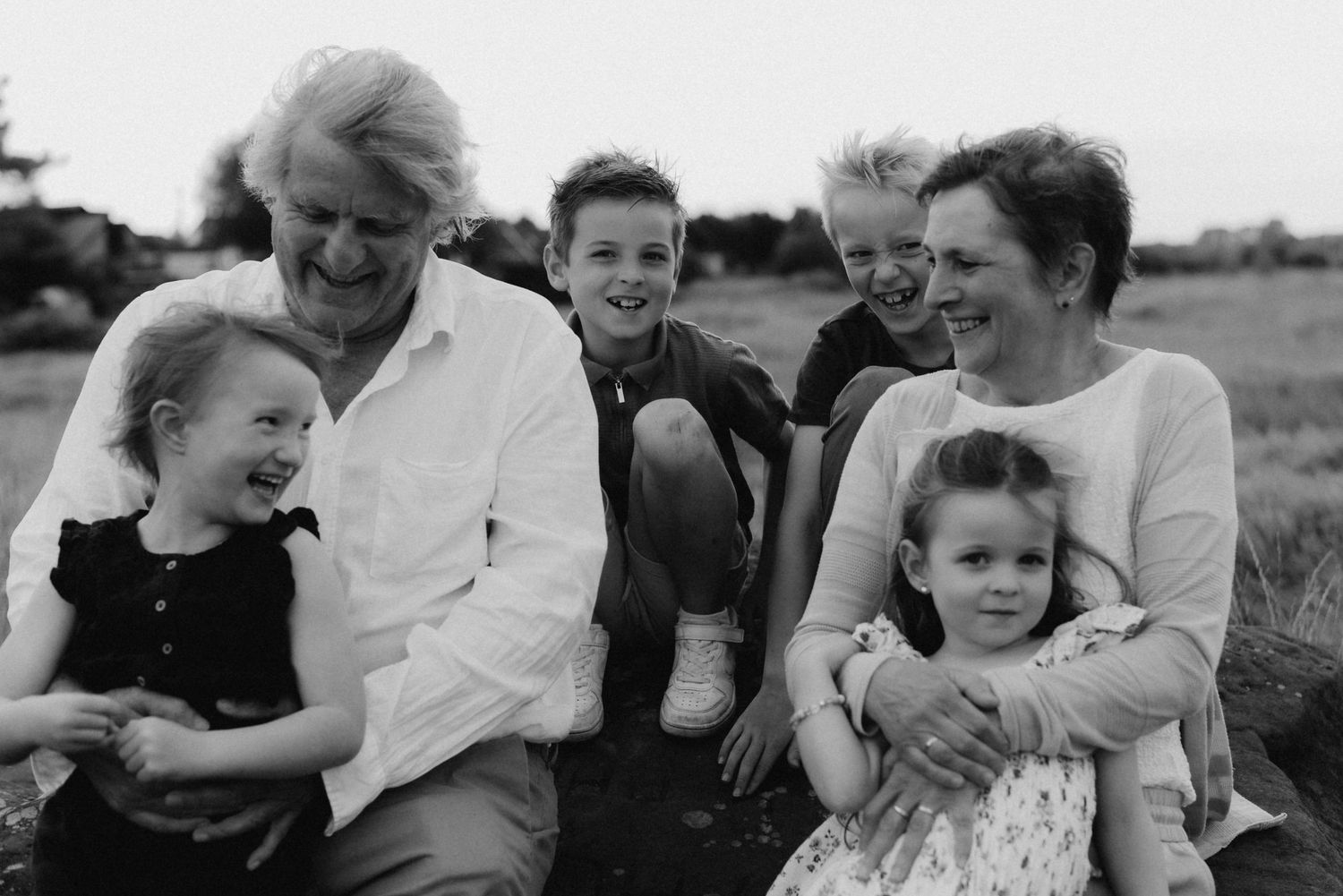 Black and white family photo of grandmother, mother, and four children laughing together outdoors in a field.