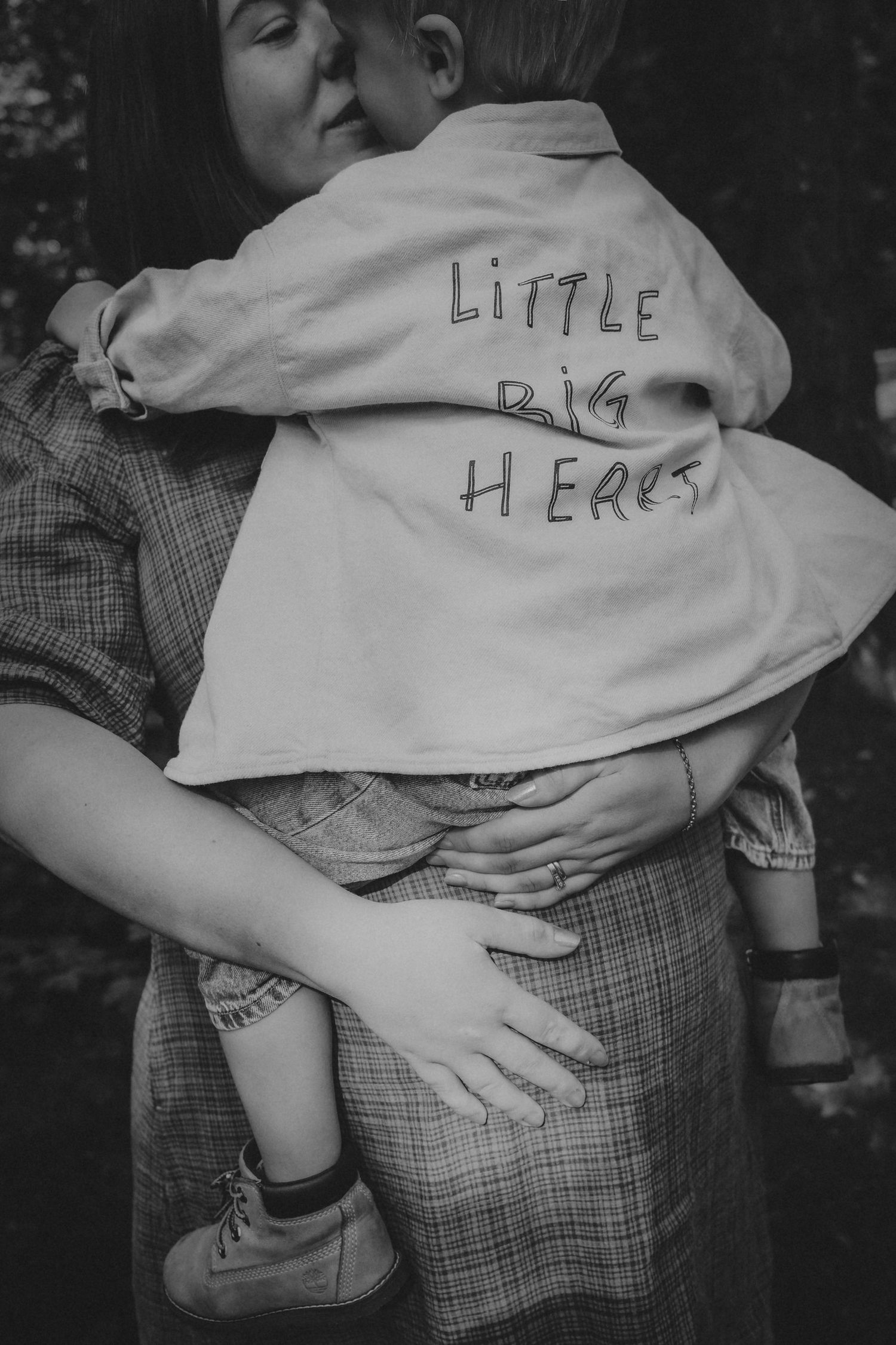 Black and white photo of a mother holding a child wearing a jacket that reads Little Big Hero.