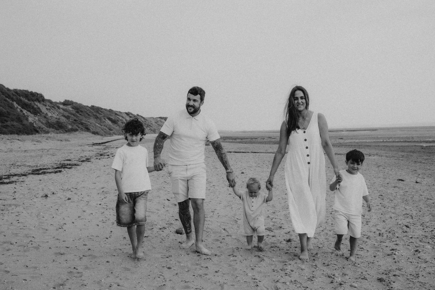 Black and white photo of a happy family of five walking on a sandy beach together.