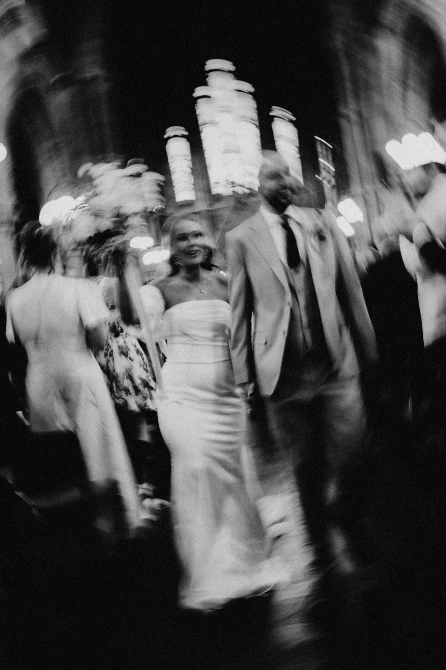 Black and white blurred photo of smiling bride in strapless gown and groom in suit at wedding reception.