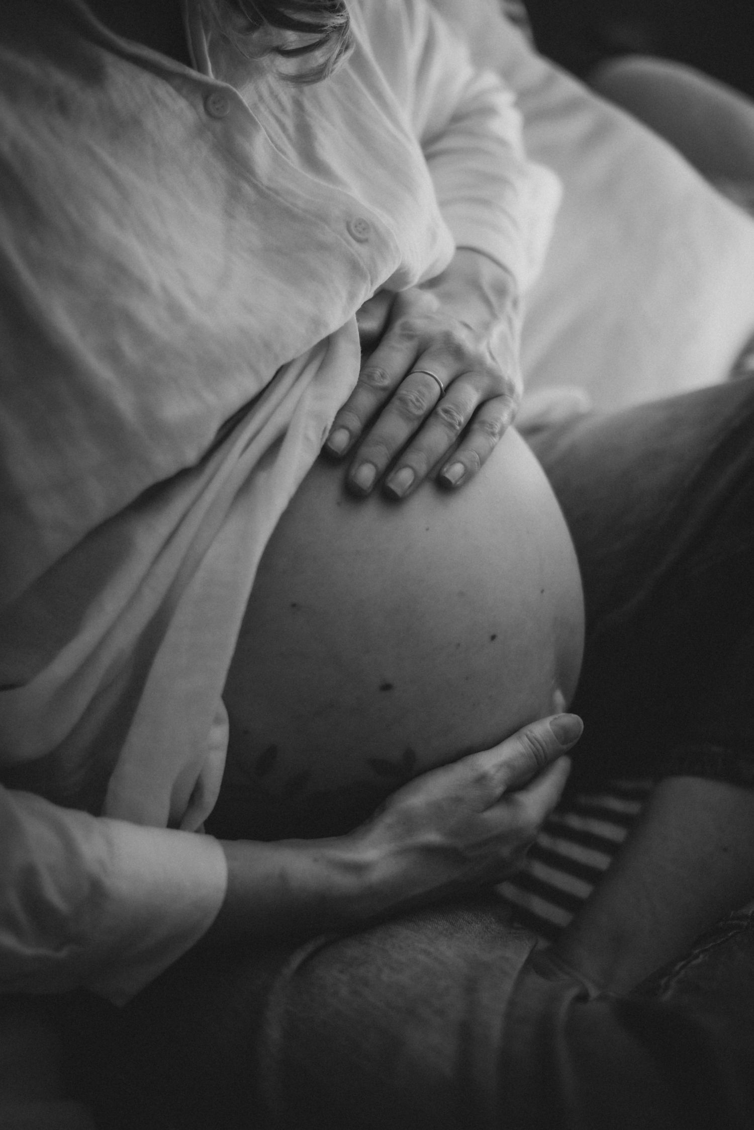 Black and white photo of pregnant woman cradling baby bump with both hands, wearing white shirt.