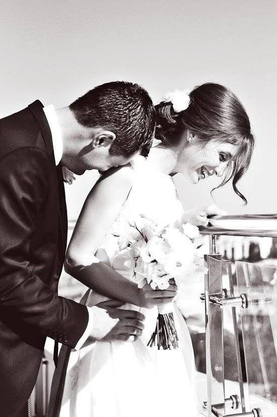 Black and white photo of a bride holding a bouquet and groom leaning in close, sharing an intimate moment at their wedding.