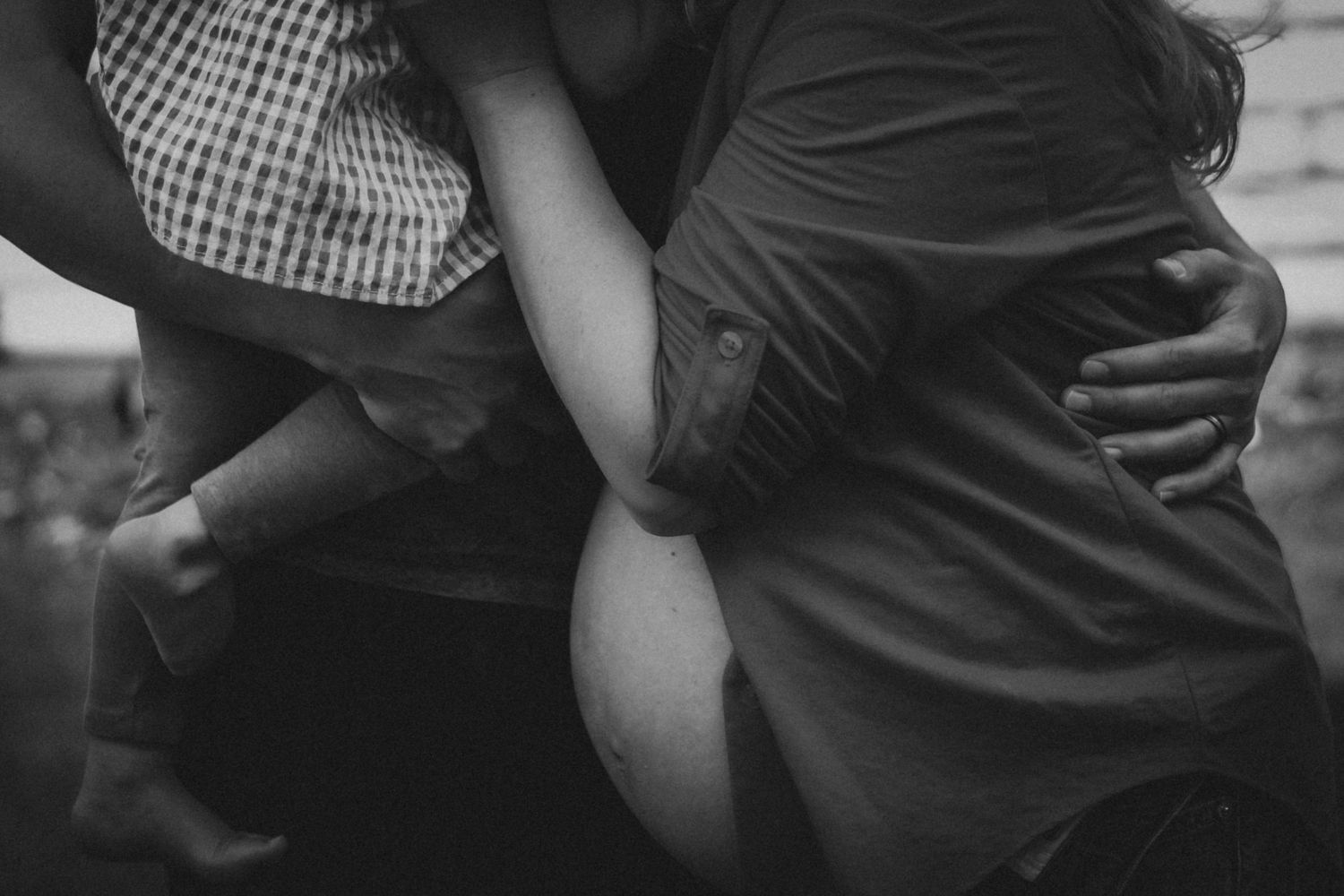 Black and white photo of a couple embracing tenderly, with one partner holding a child, capturing a warm family moment.