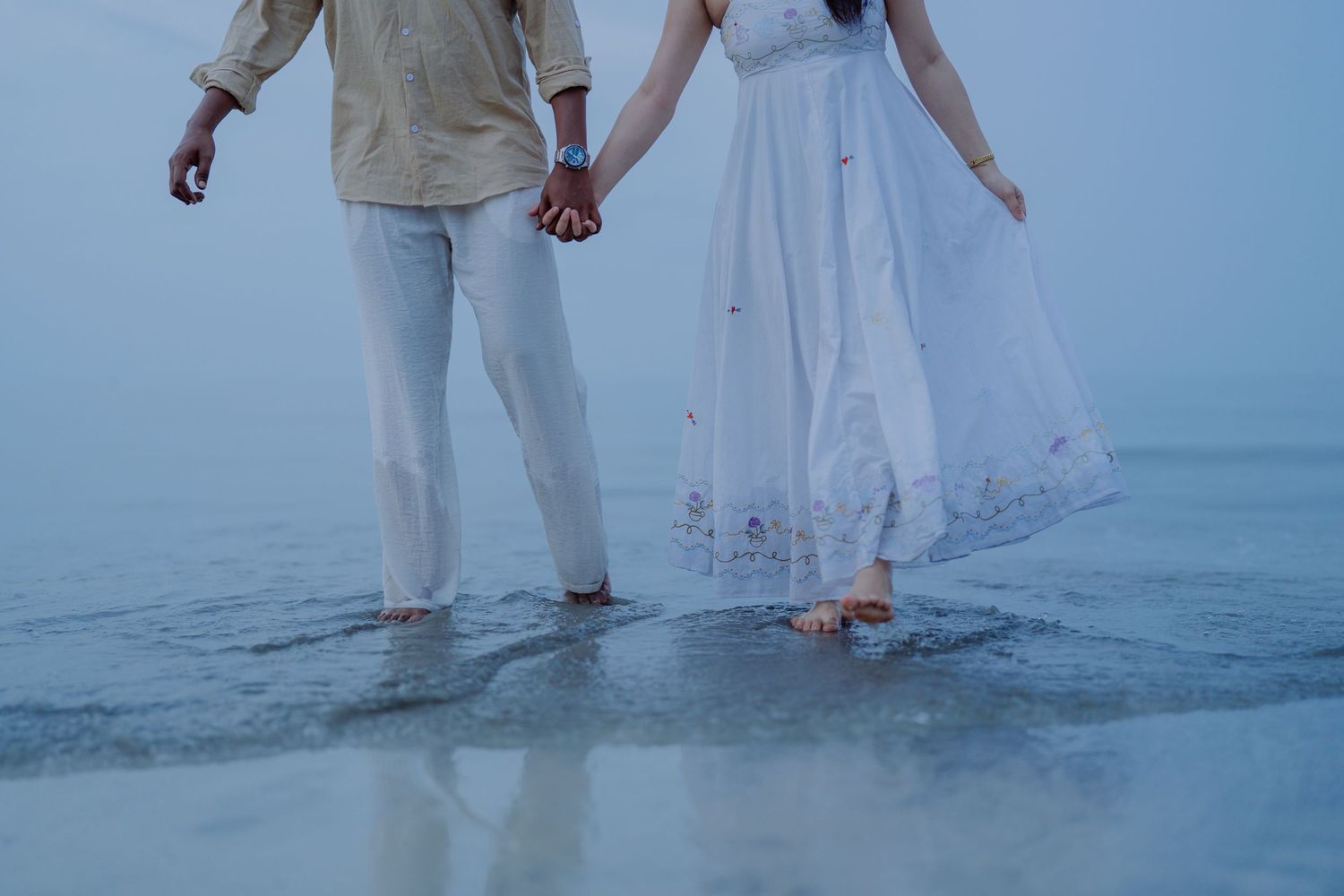Couple walking hand in hand along the shoreline during a seaside engagement photoshoot.