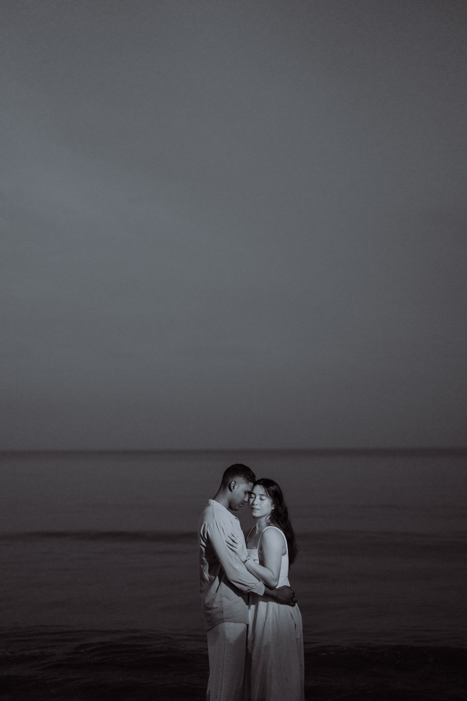 Intimate beach portrait of a couple embracing by the sea, captured in a timeless and cinematic style.