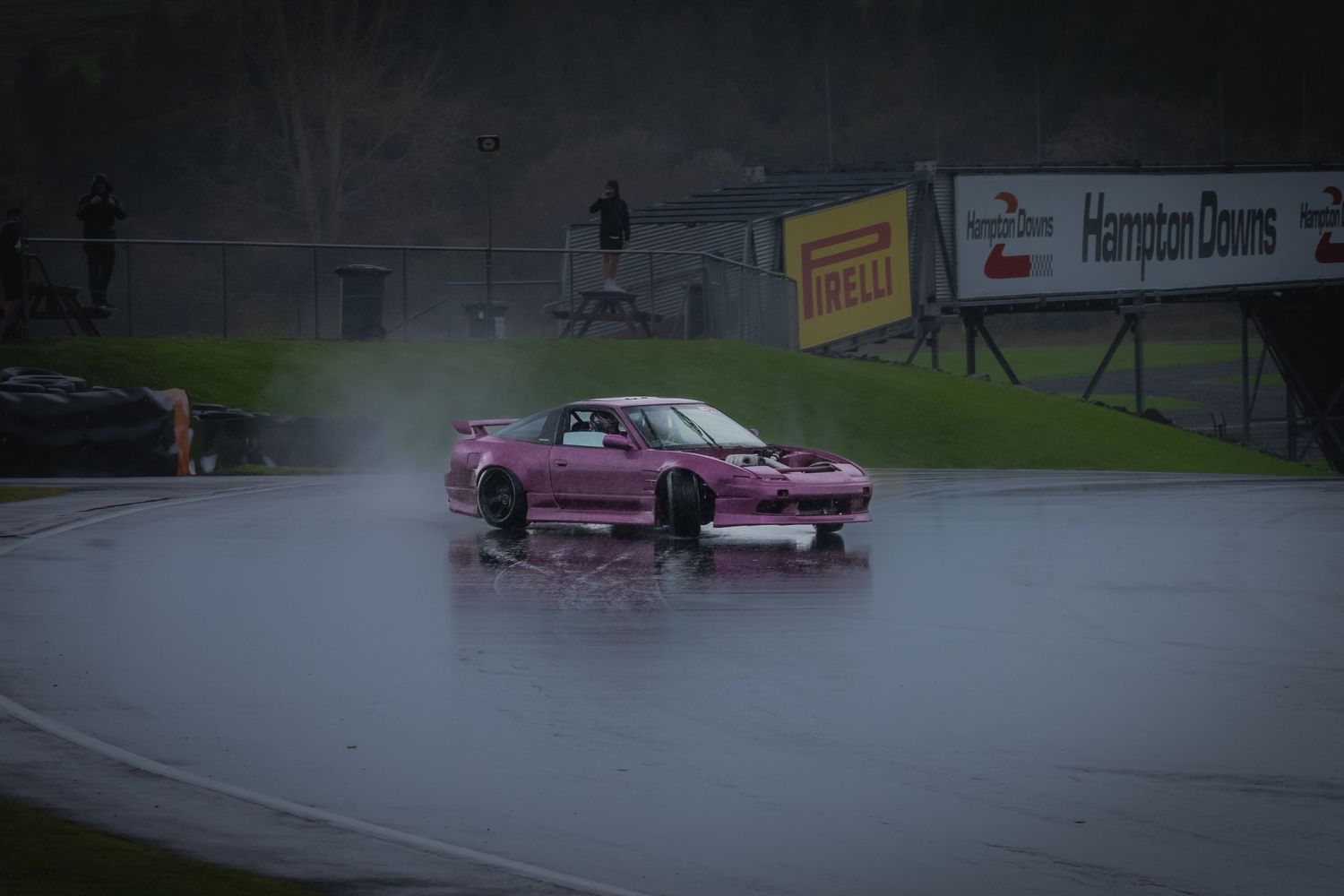 Pink sports car drifting on wet race track in rainy conditions at Hampton Downs motorsport park.